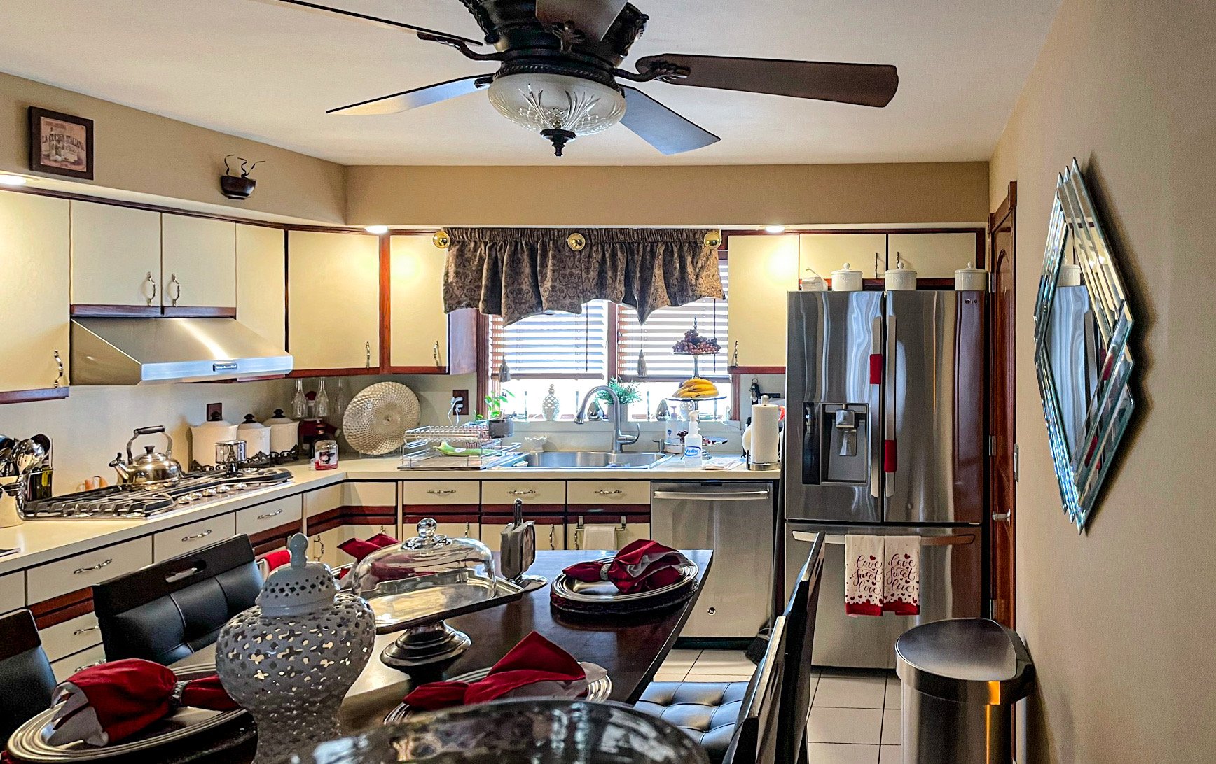 Cozy kitchen with beige cabinets, stainless steel refrigerator, and a dining table set with red napkins and festive decorations.