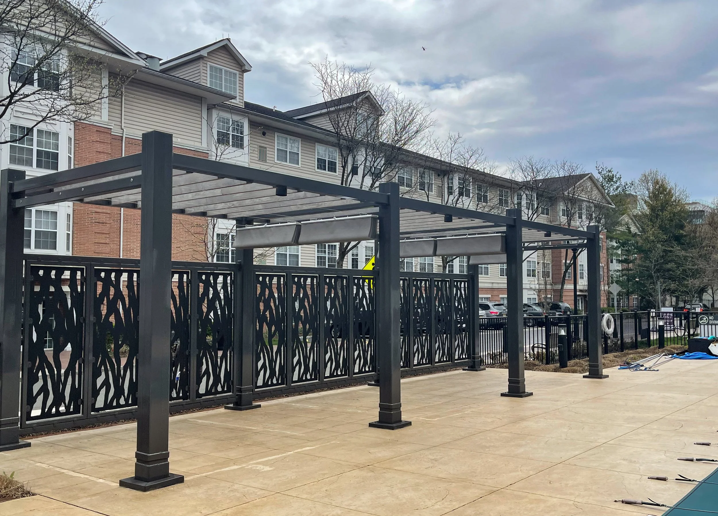 Outdoor structure with a metal frame and decorative black metal fence panels on a concrete surface, near a residential apartment complex.