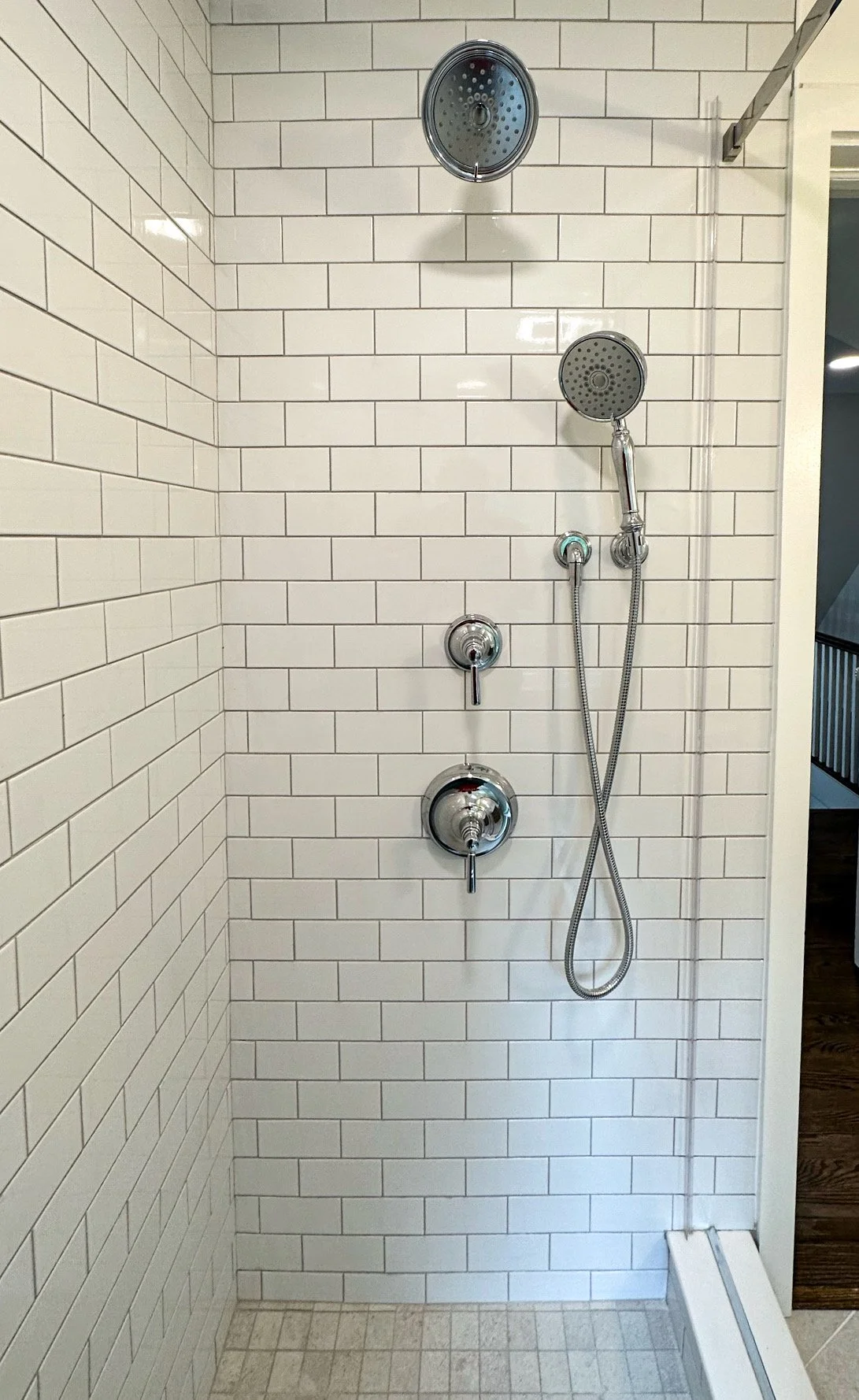 Bathroom shower area with white subway tile walls, two showerheads, a handheld shower, and water control knobs.