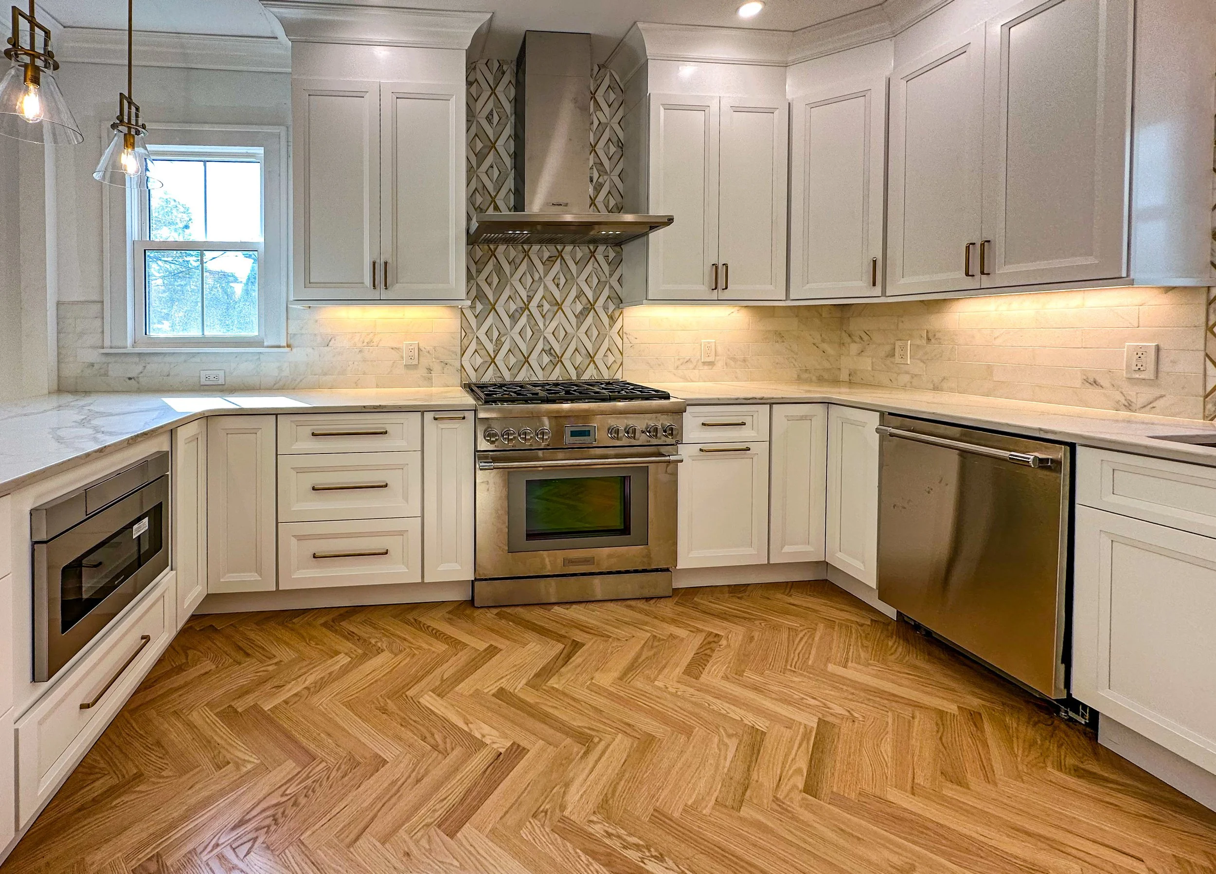 A modern kitchen with white cabinets, stainless steel appliances, and wooden herringbone floor.
