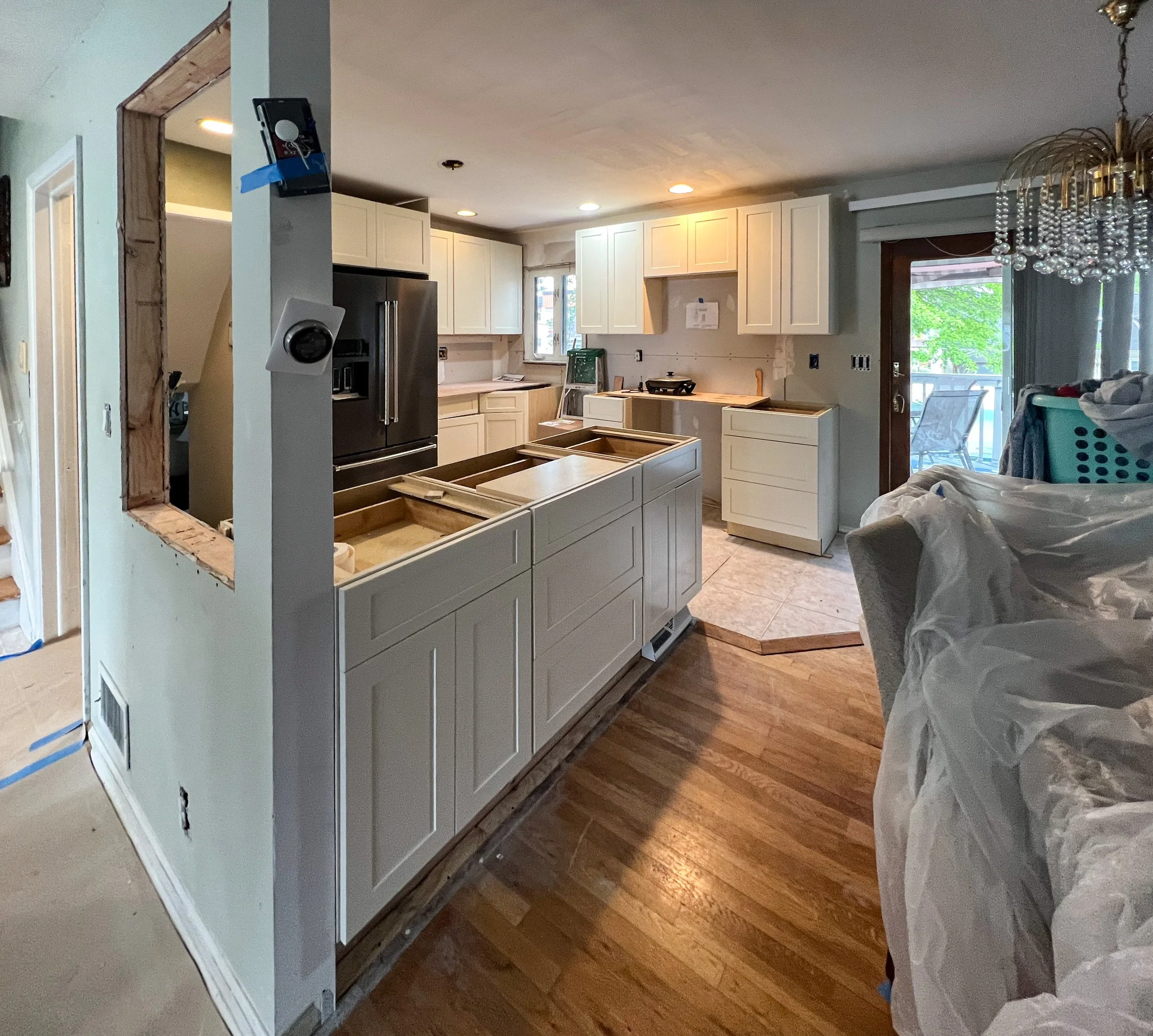 Kitchen undergoing renovation with white cabinets, dark refrigerator, wooden countertops, and a sliding glass door leading outside.