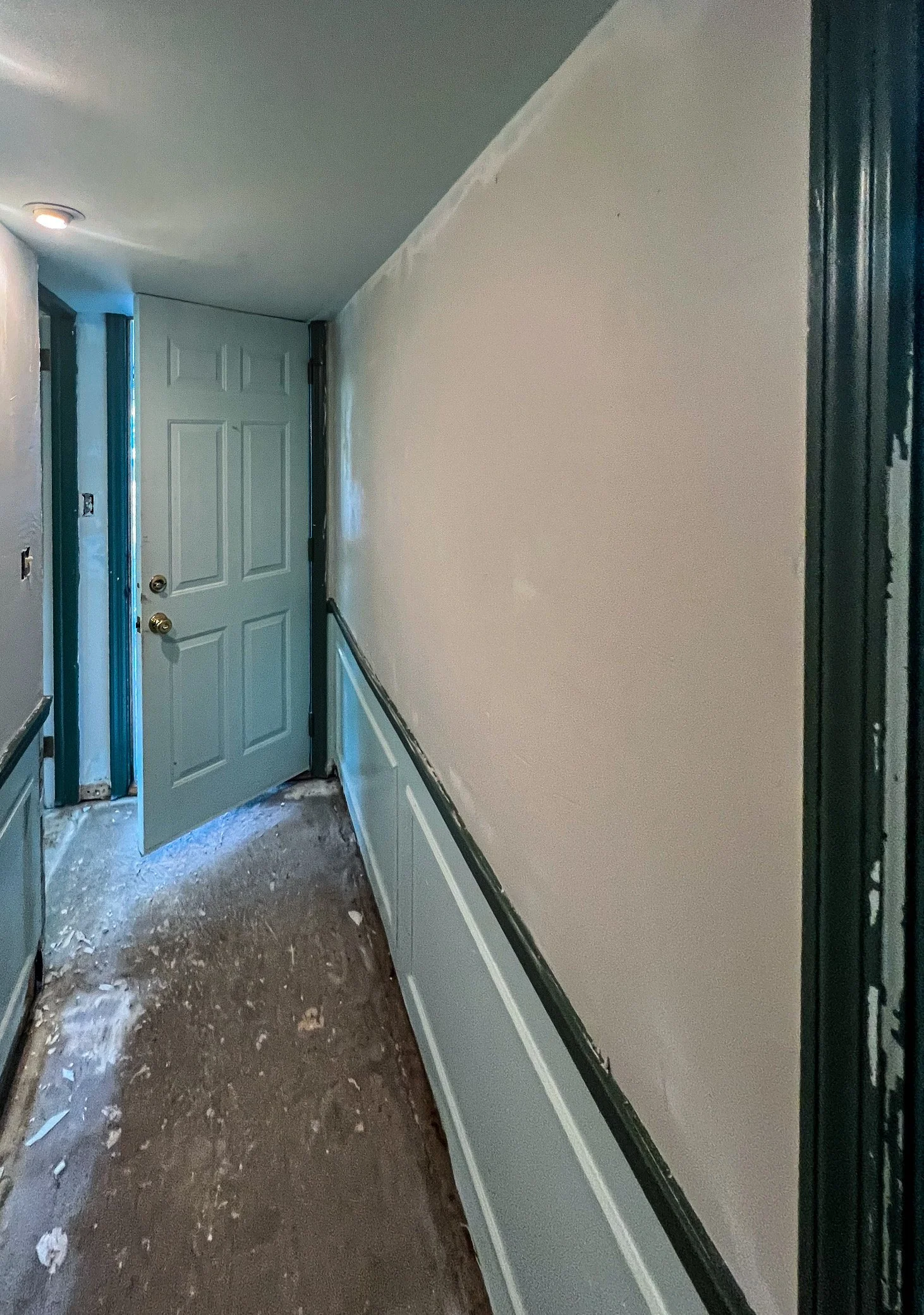 A hallway under renovation with a partially open door at the end, walls partially painted, and construction debris on the floor.