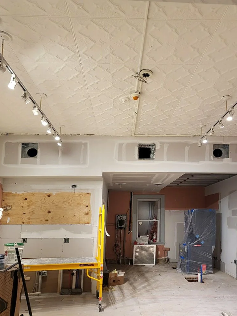 An interior room under renovation with exposed wiring, drywall, and construction tools.