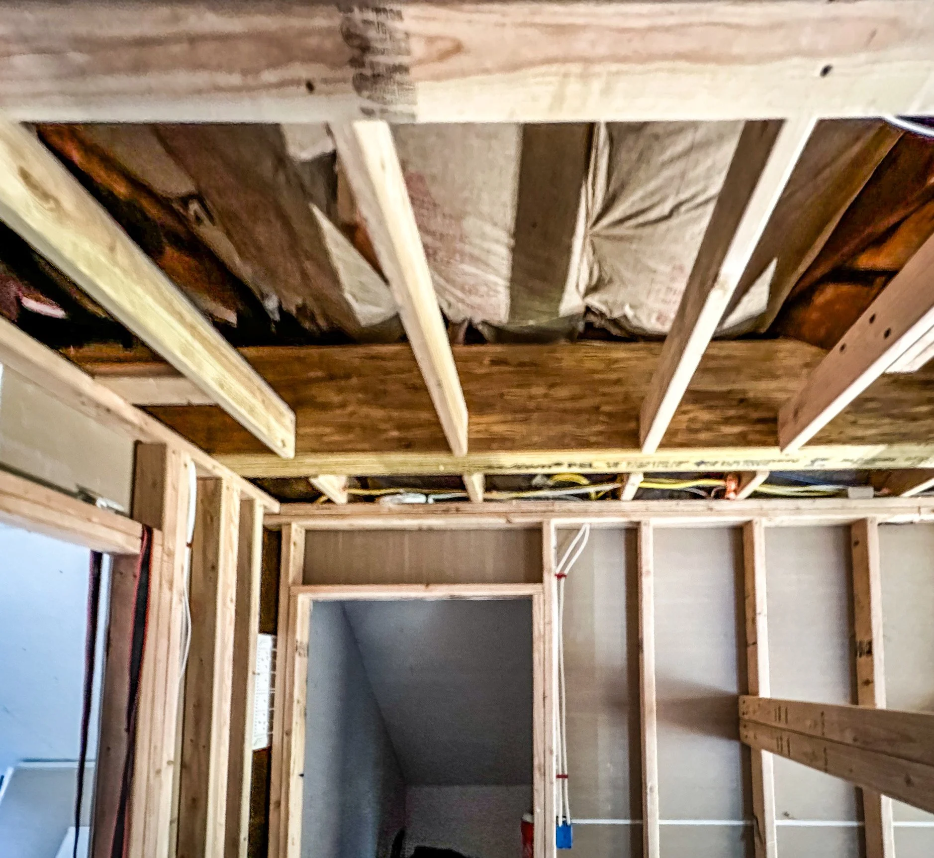 Interior wall framing under construction with exposed wooden studs and insulation on the ceiling.