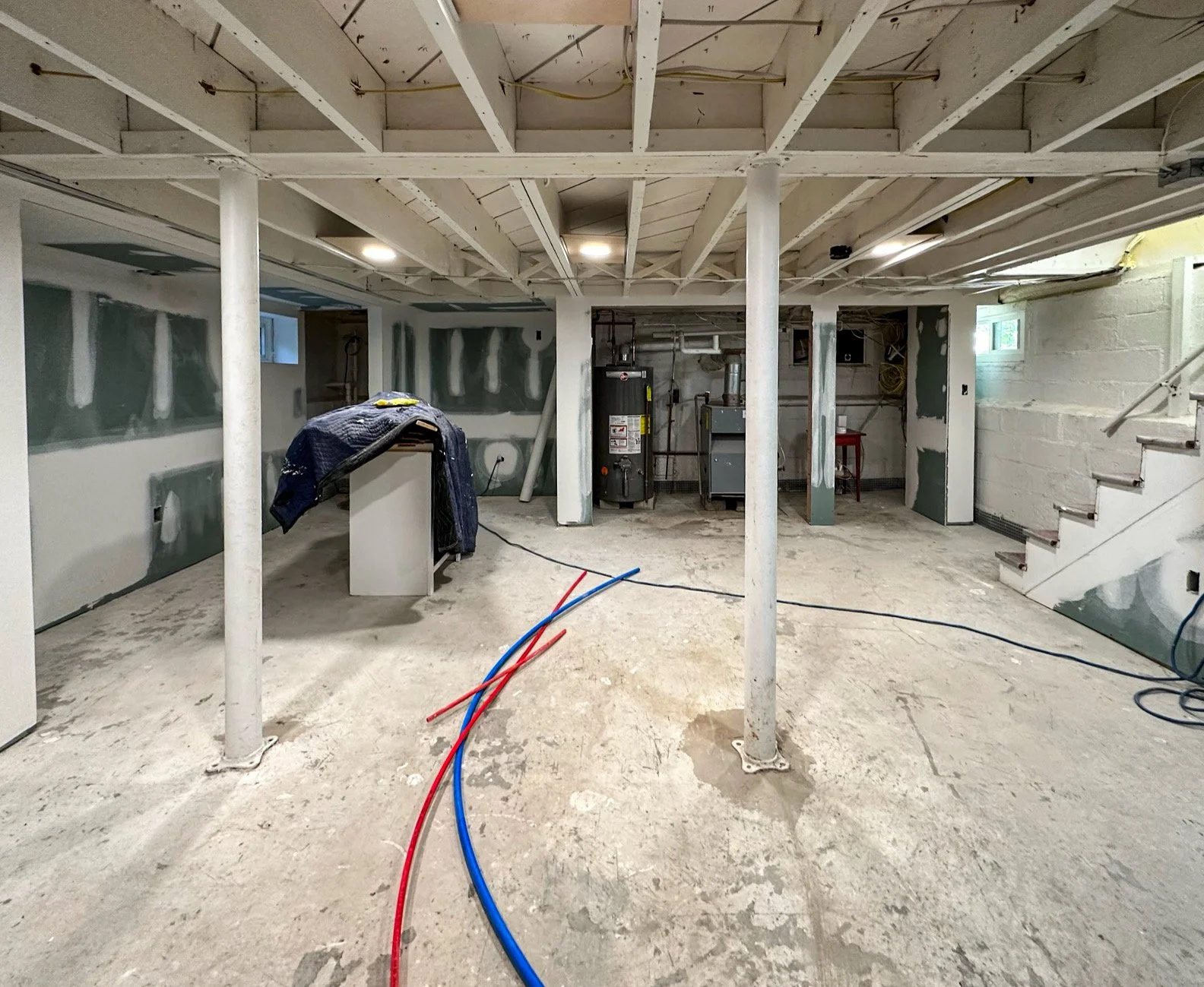 Basement under construction with exposed pipes, unfinished walls, and support columns.