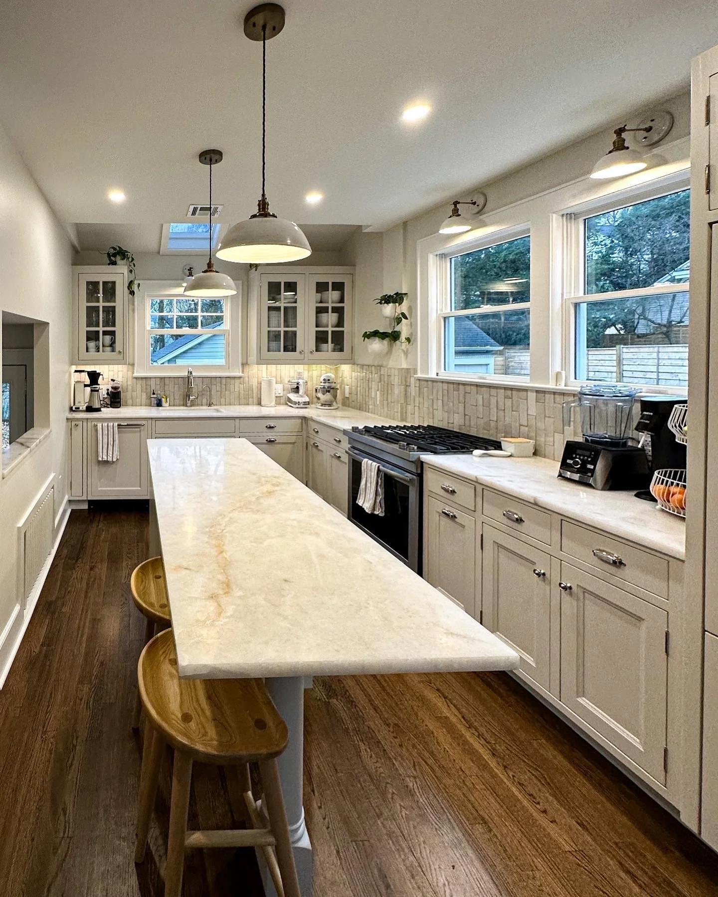 Bright kitchen with white cabinetry, large windows, hardwood floors, and a marble island countertop with two wooden stools.