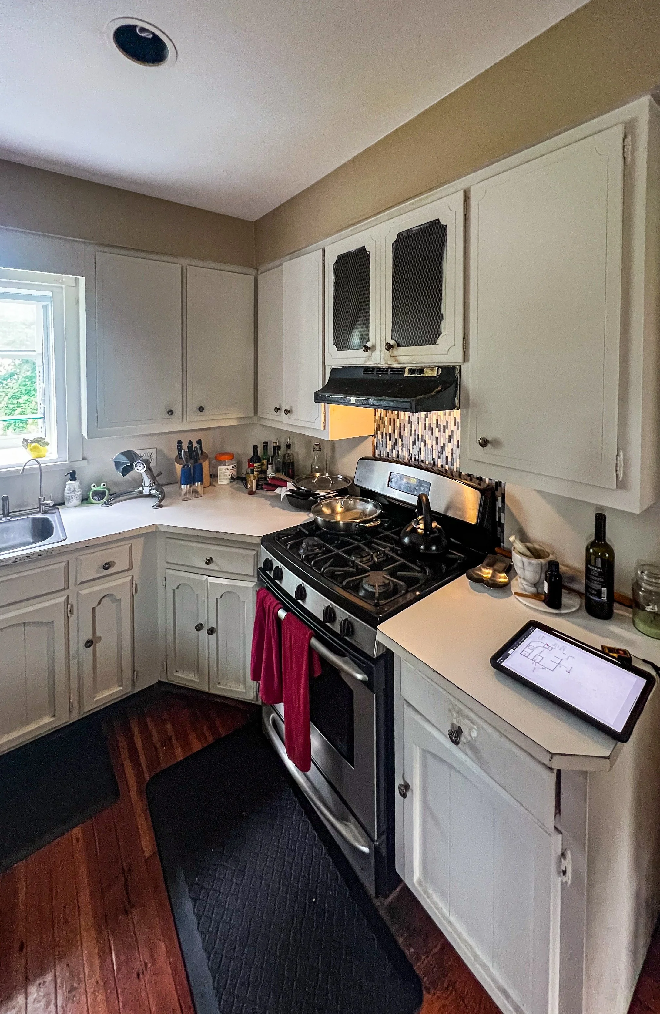 A kitchen with white cabinets, a window, a stove with a red towel hanging, and various kitchen items on the countertops.