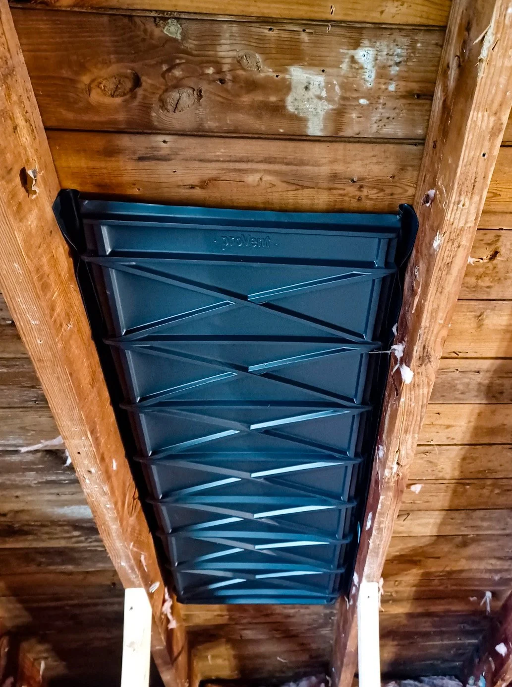 A new attic attic ventilation fan installed between wooden beams in the ceiling.