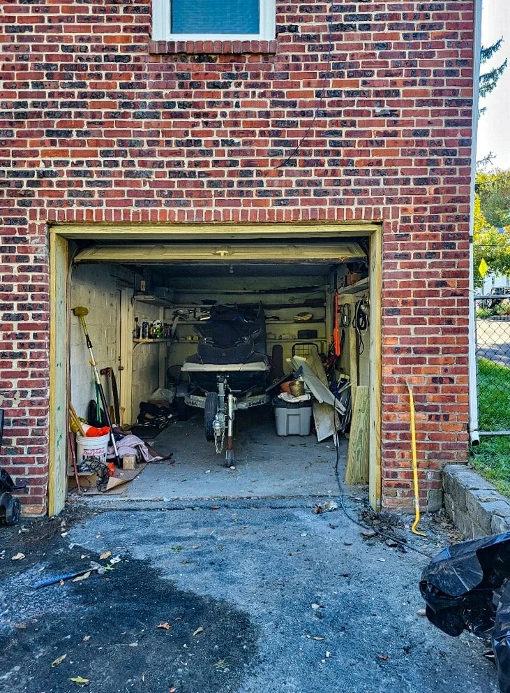 A garage inside a brick building with the door open, containing a boat, tools, and storage bins.