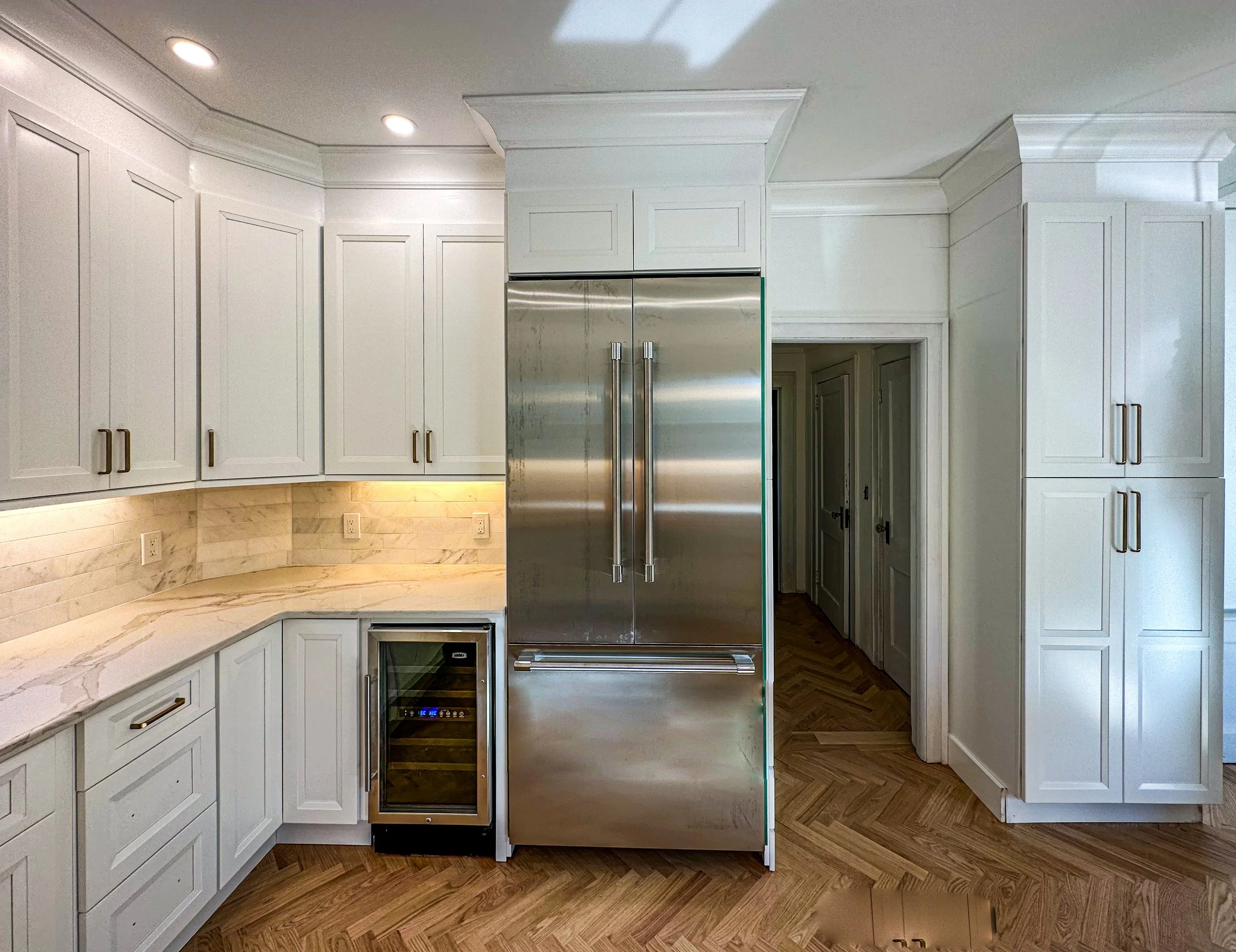 Modern kitchen with white cabinets, marble countertop, a built-in wine cooler, and a large stainless steel refrigerator.