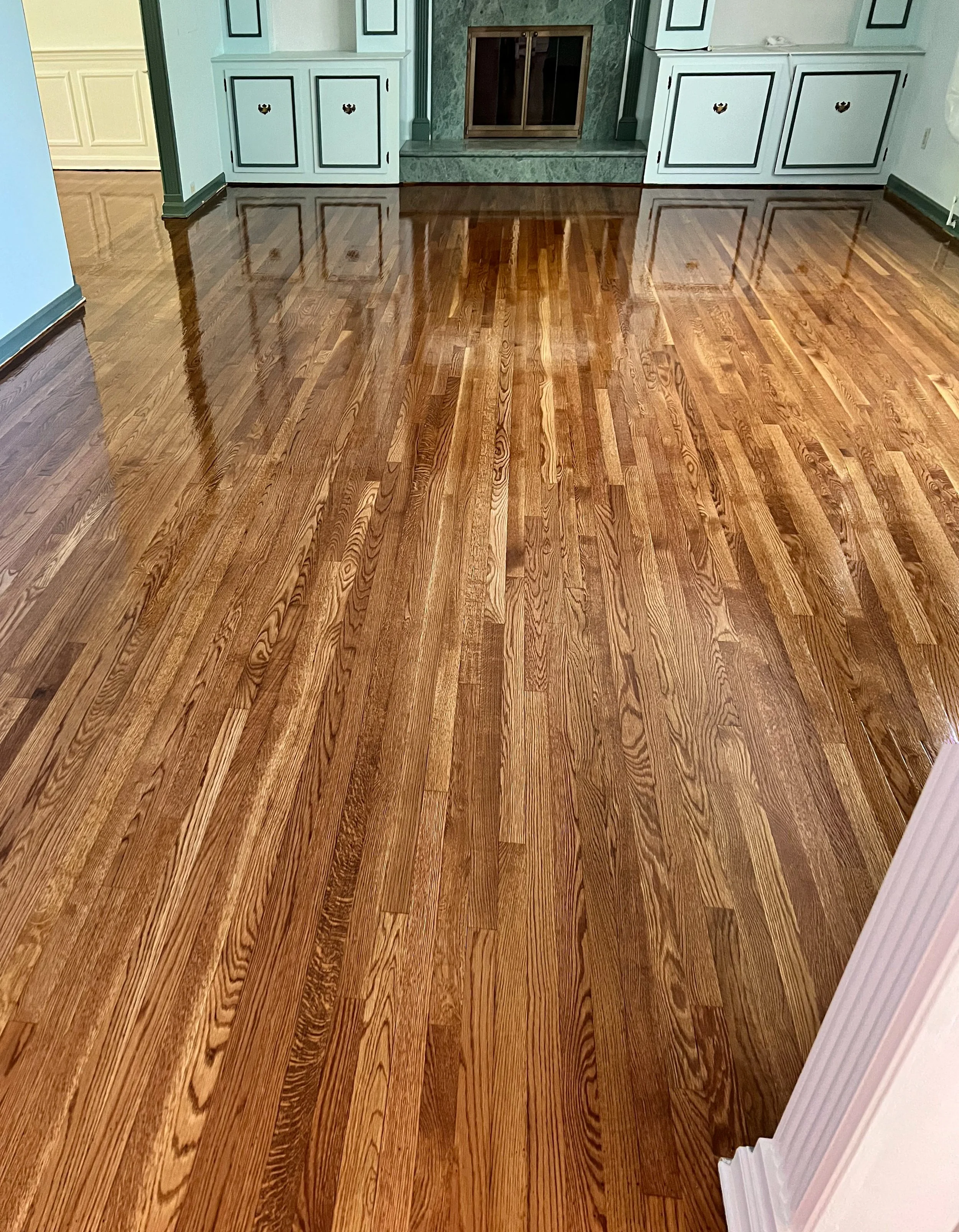 Polished hardwood floor in a living room with a fireplace and built-in cabinets.