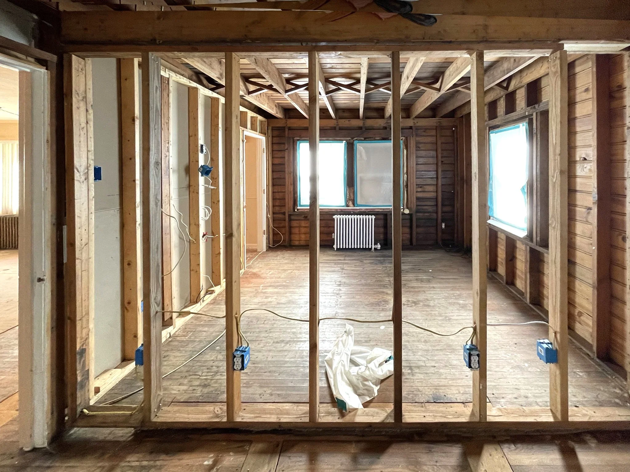 Room under construction with wooden framing, exposed walls, and windows covered with protective plastic.