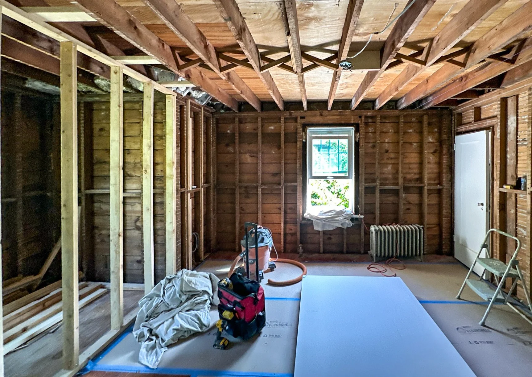 Interior of a room under renovation with exposed wooden framing, a window, and construction tools and materials on the floor.