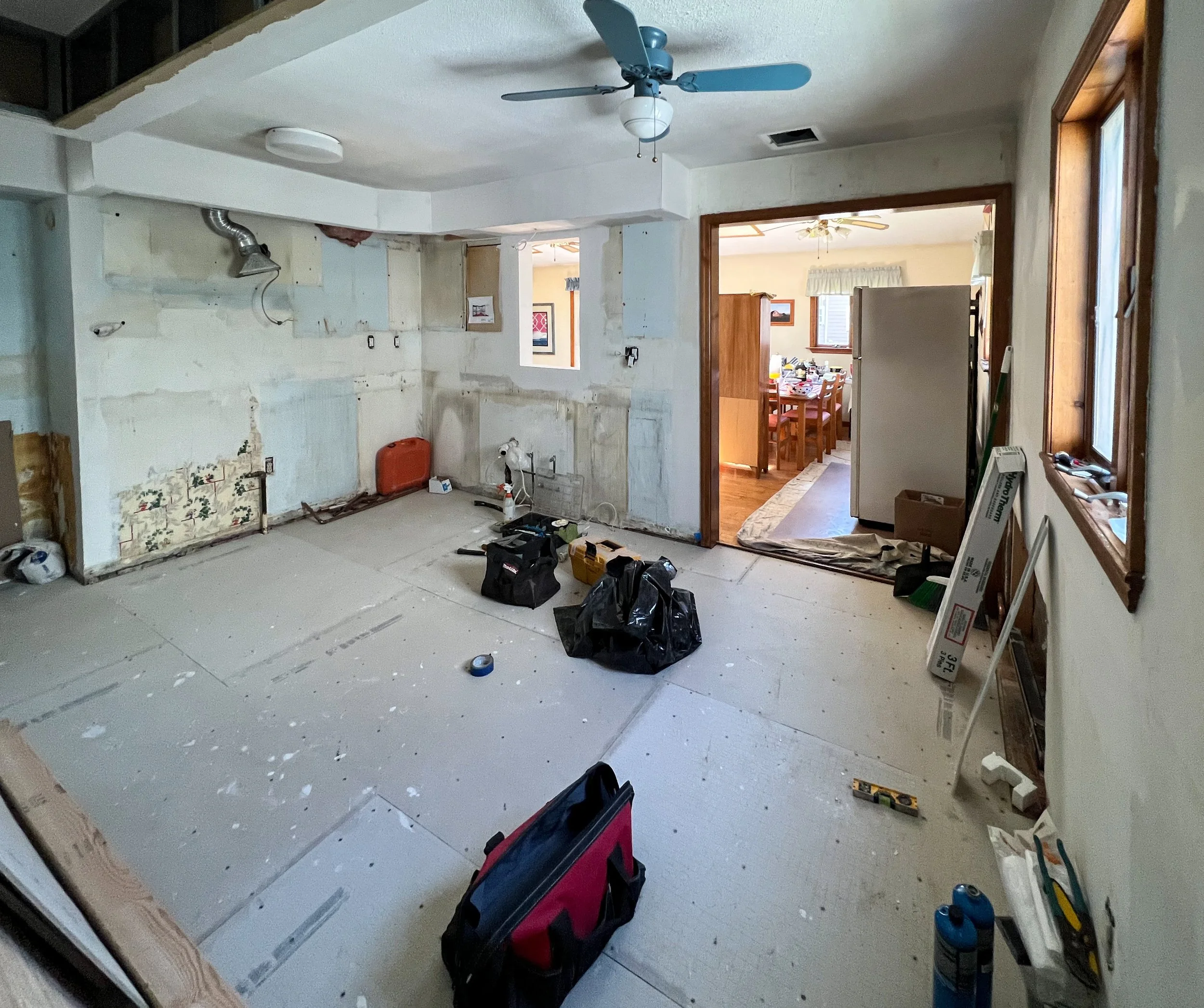 Room under renovation with tools and construction materials scattered around, partially stripped walls, and an opening to a dining area.
