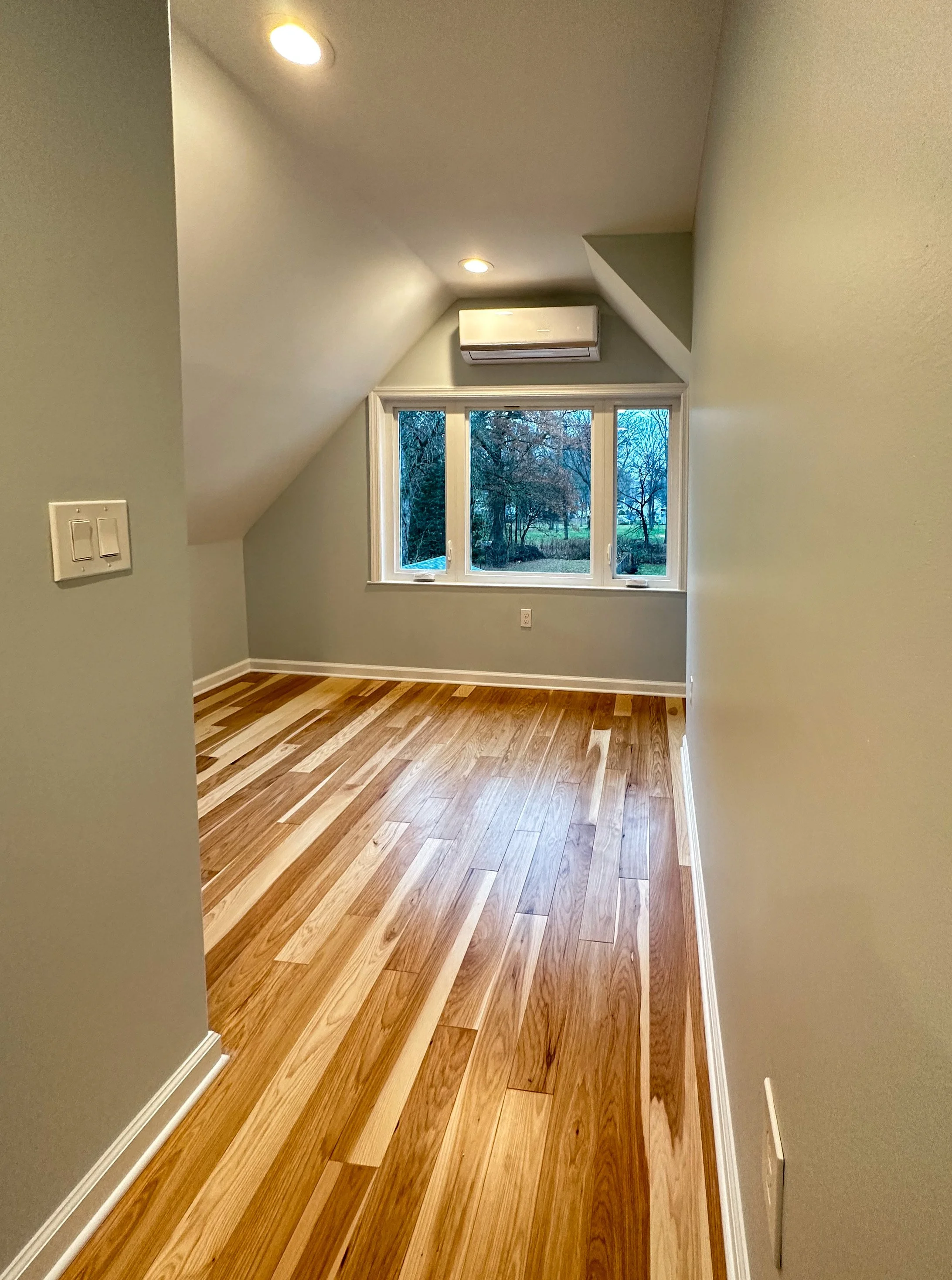 Empty room with wooden flooring, a large window, and an air conditioning unit on the wall.