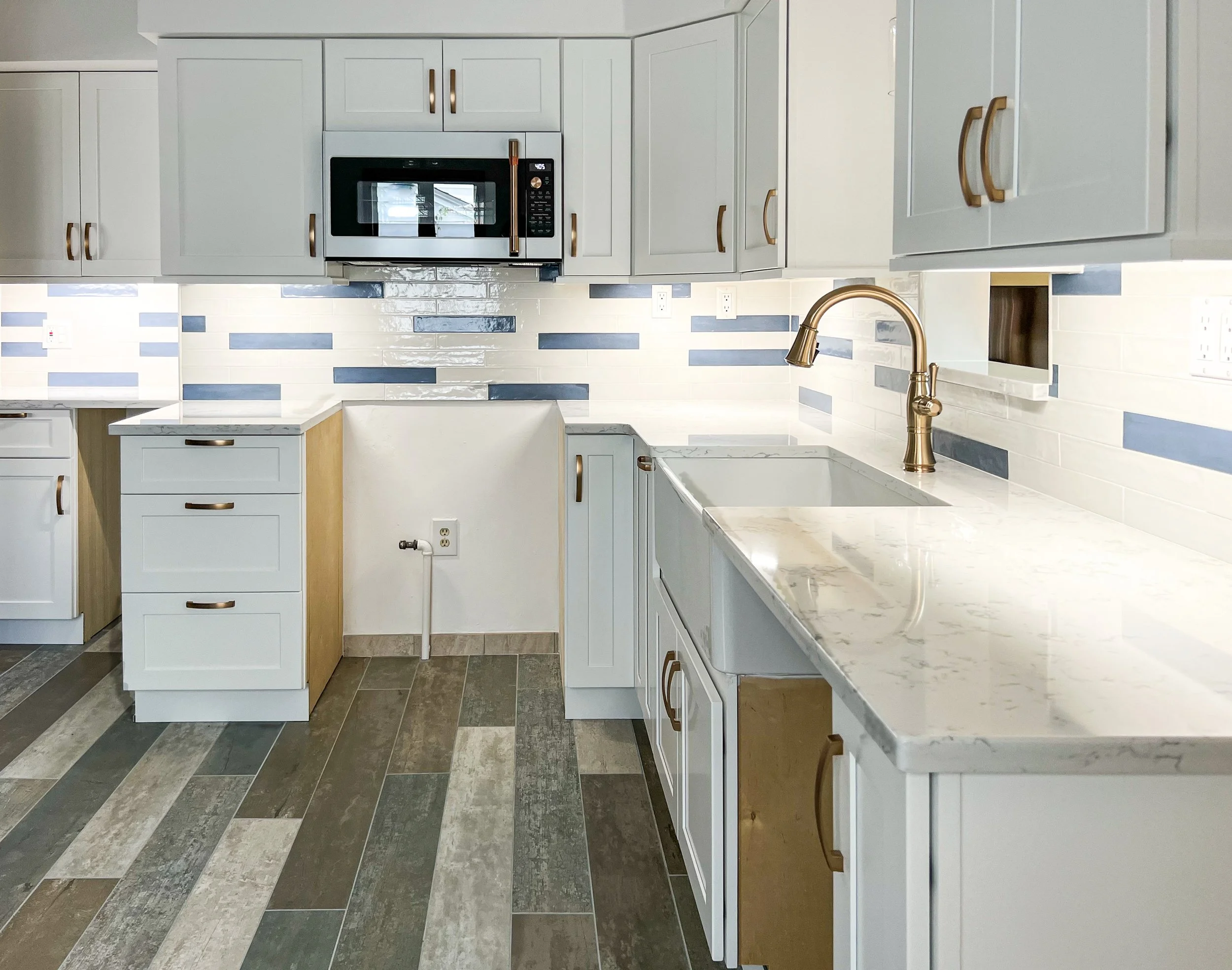 Modern kitchen with white cabinets, marble countertops, yellow and white drawers, brass faucet, and a colorful tiled backsplash.