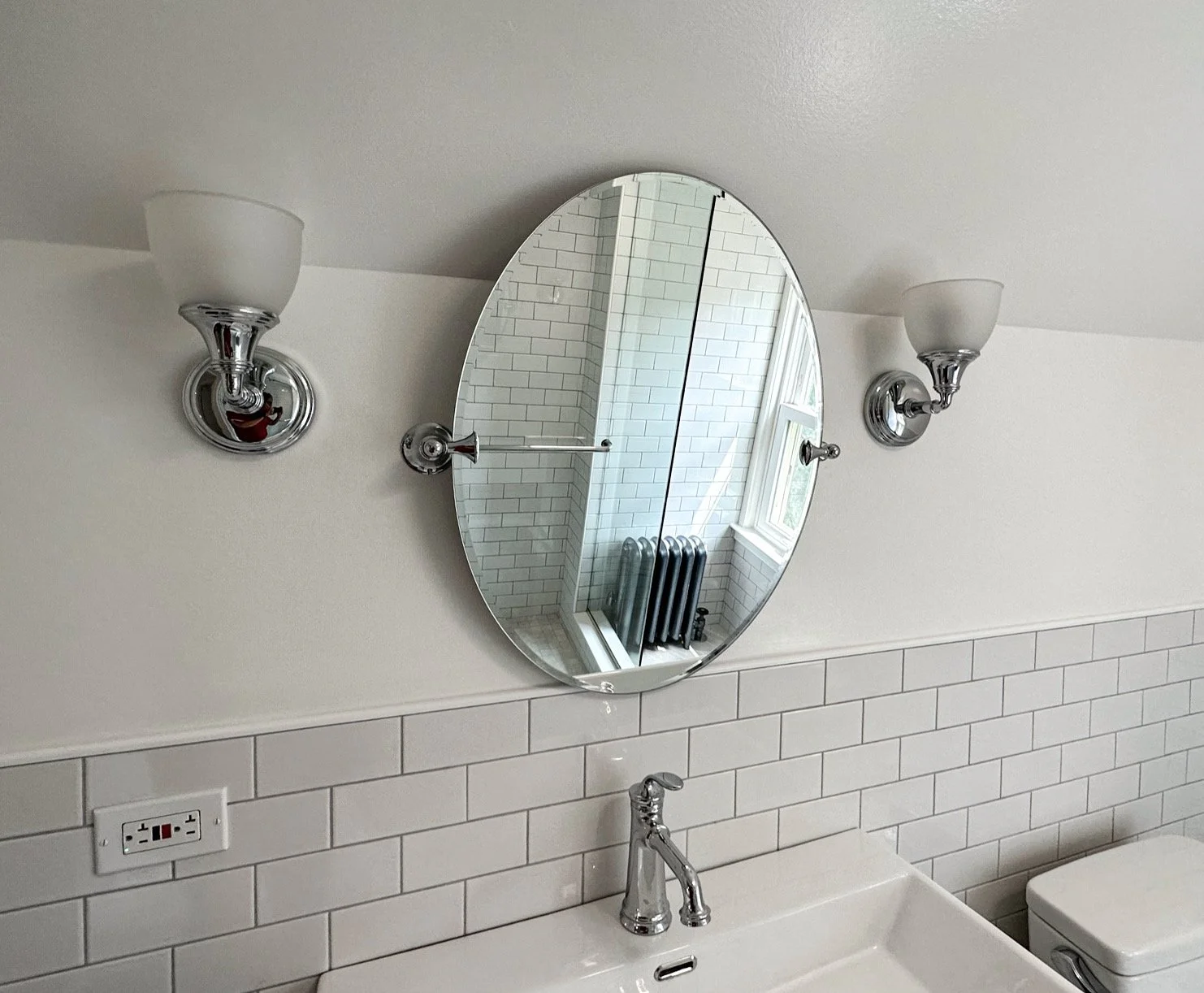 Bathroom with white subway tile walls, a round mirror, two wall-mounted light fixtures, a faucet, and a partially visible washing machine.