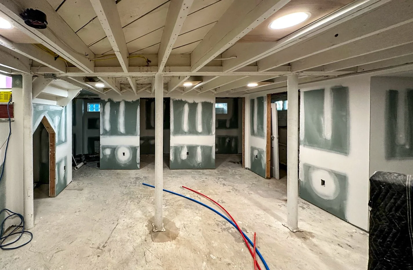 Interior of a room under construction with drywall partially installed, visible electrical wiring, and exposed ceiling beams.