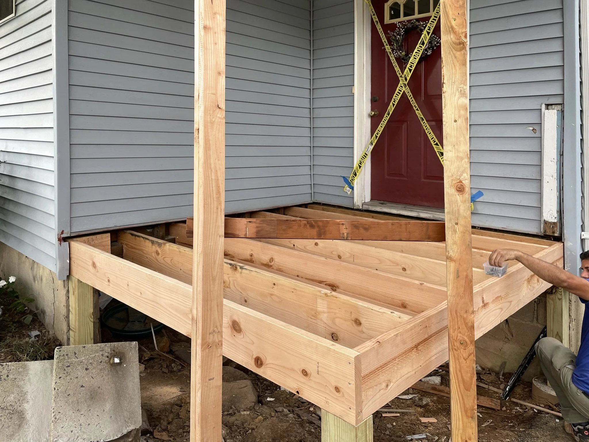 Construction of a new wooden porch in front of a house with blue siding and a red door, with yellow caution tape across the doorway.