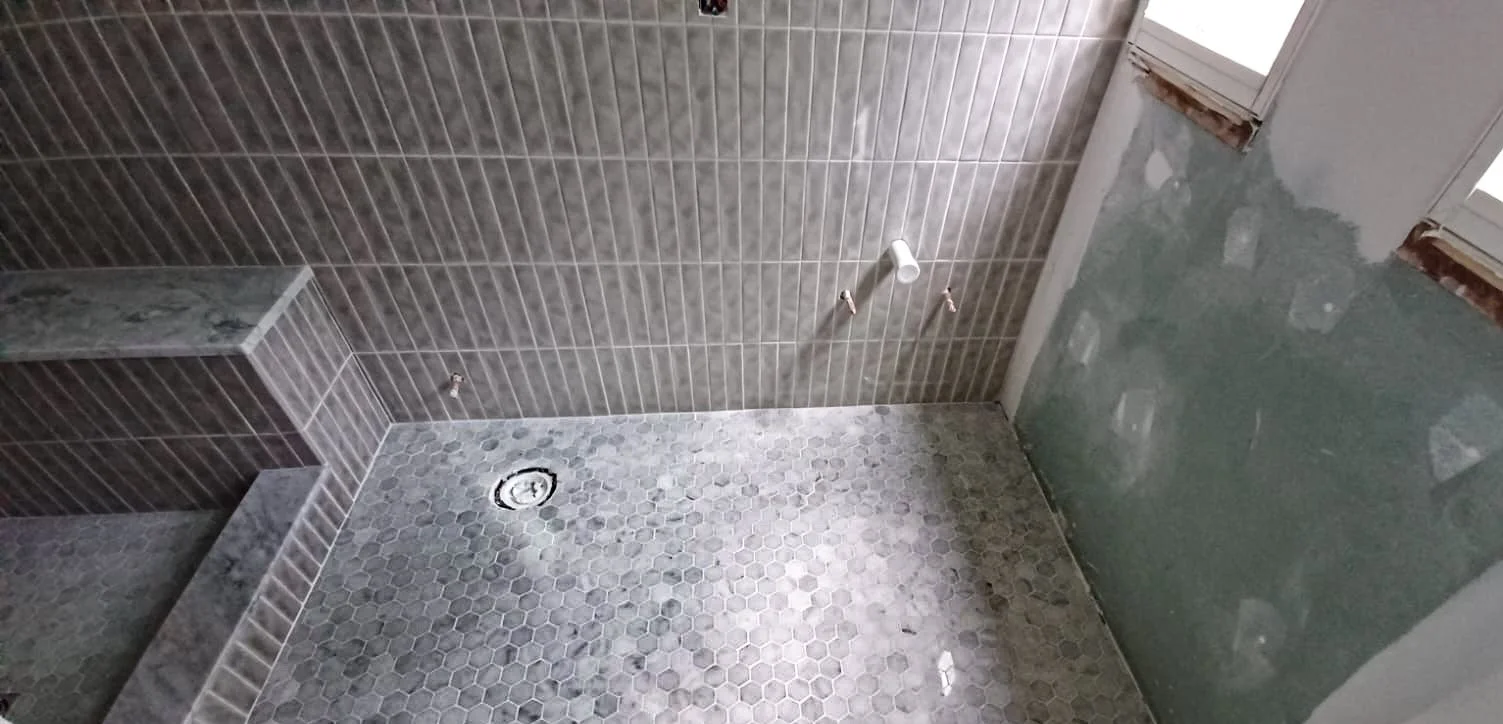 Bathroom under renovation with uninstalled bathroom fixtures, unfinished tiled wall and floor, and roofing window.