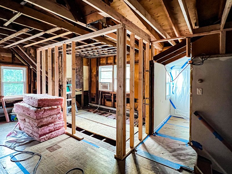 Interior of a house under renovation with exposed wooden framing, insulation, and construction materials.