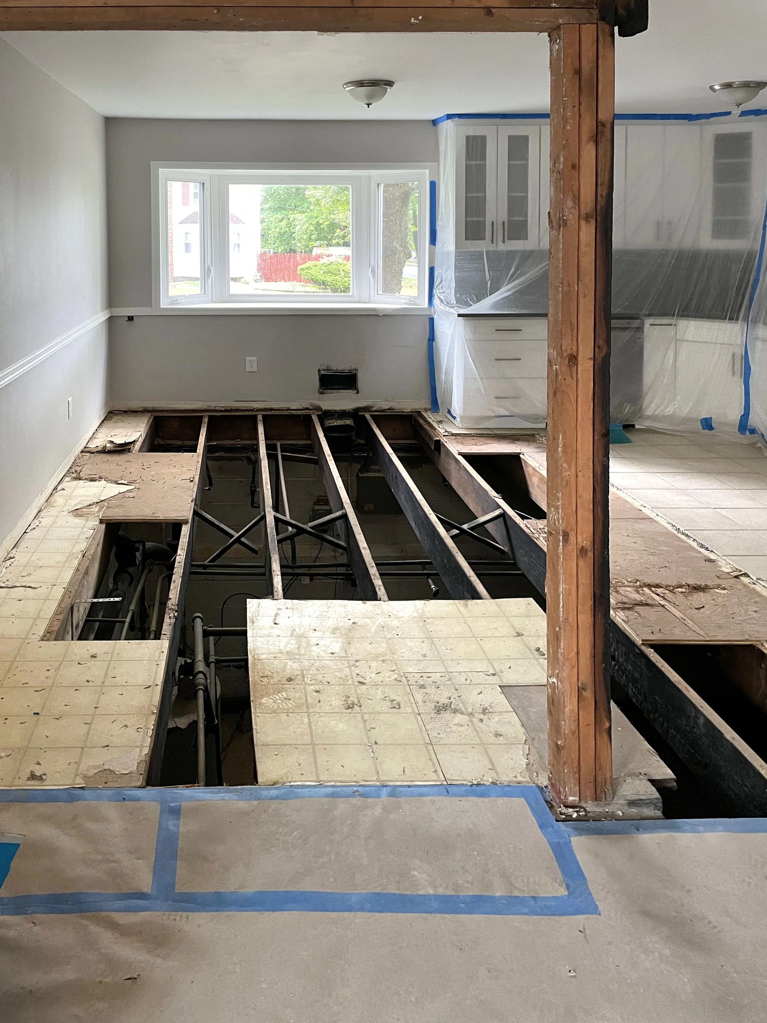 Kitchen with subfloor and framing for new flooring, cabinets covered in plastic for renovation.