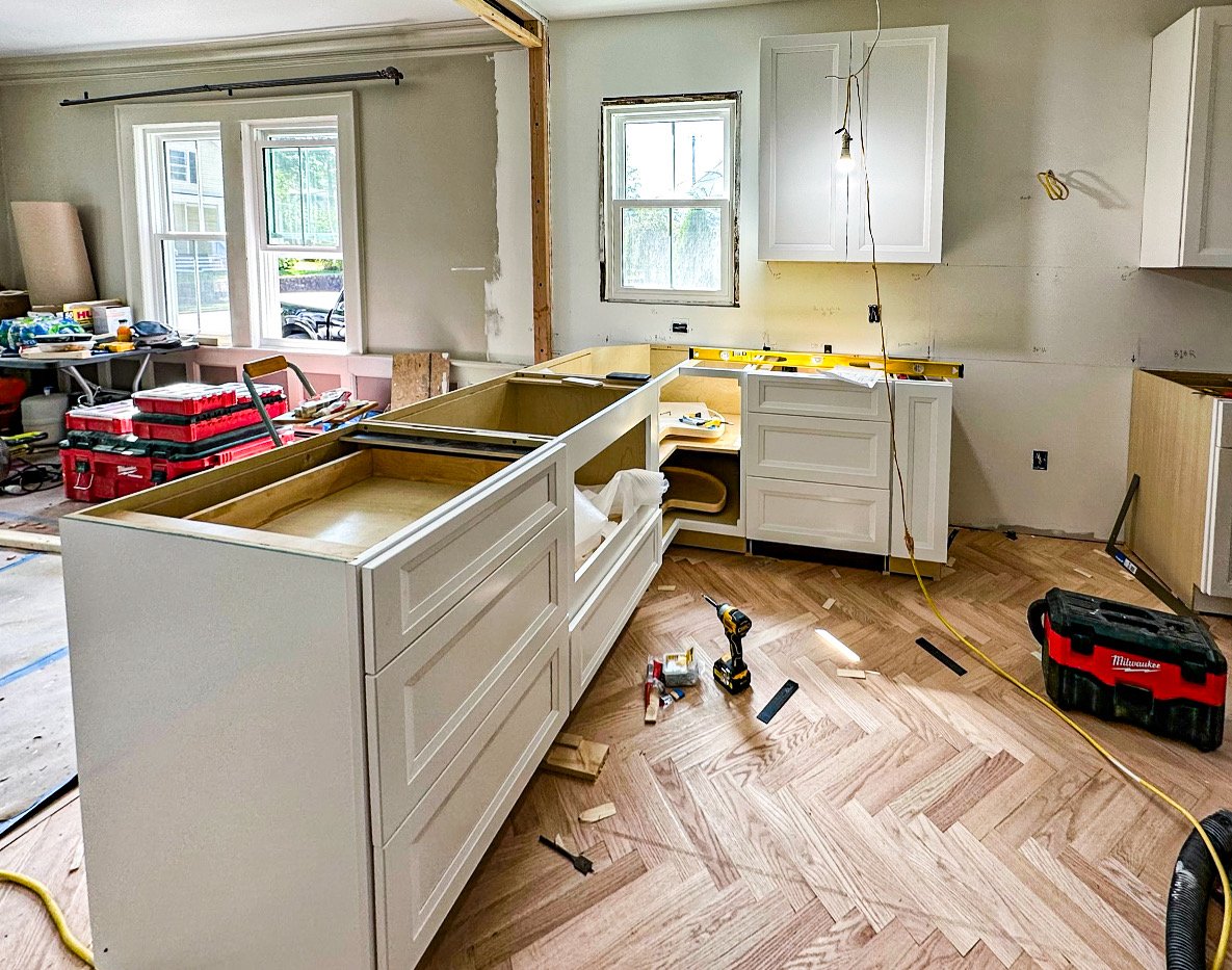 Kitchen under renovation with partially installed cabinets, construction tools, and materials scattered around.