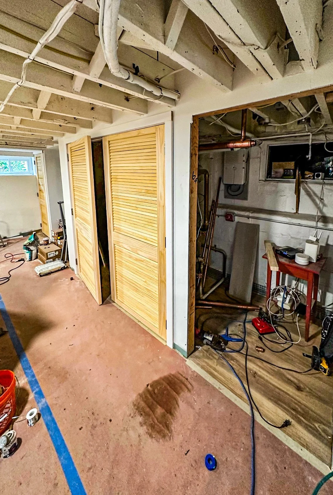 Interior of a basement under construction, with unfinished ceiling, new wooden closet doors, construction tools, and wiring.