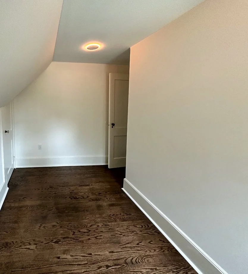 Empty room with hardwood floors, white walls, a sloped ceiling, and a door at the end