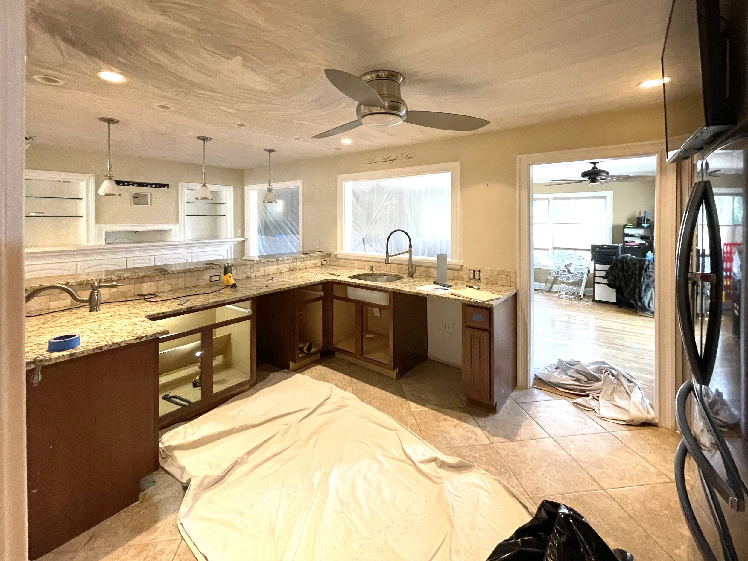 Kitchen with granite countertops, under-construction cabinets, and a ceiling fan. Adjacent room has large windows, a ceiling fan, and office equipment.