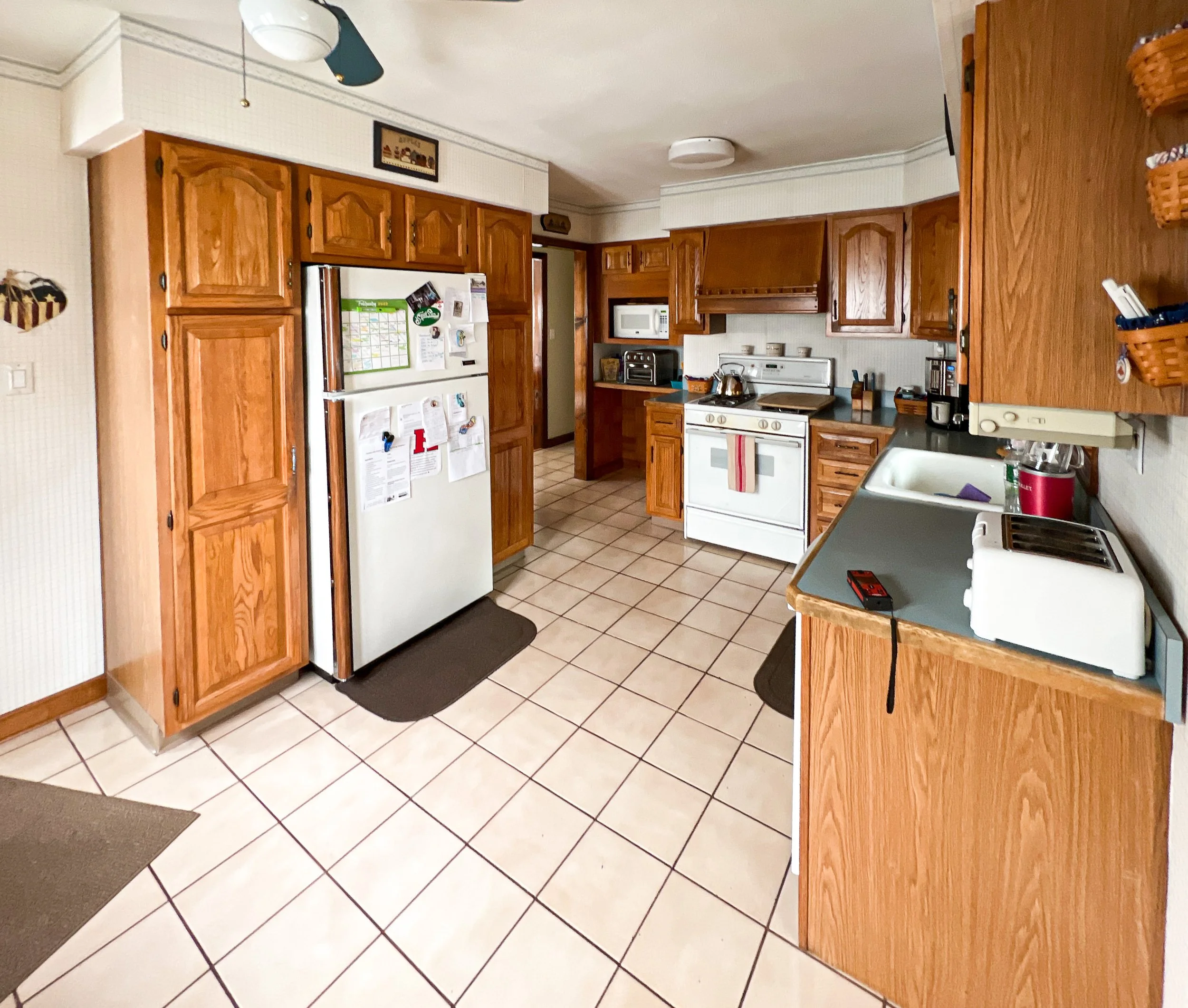 A kitchen with wooden cabinets, white appliances, a tile floor, and various kitchen items on the counters.