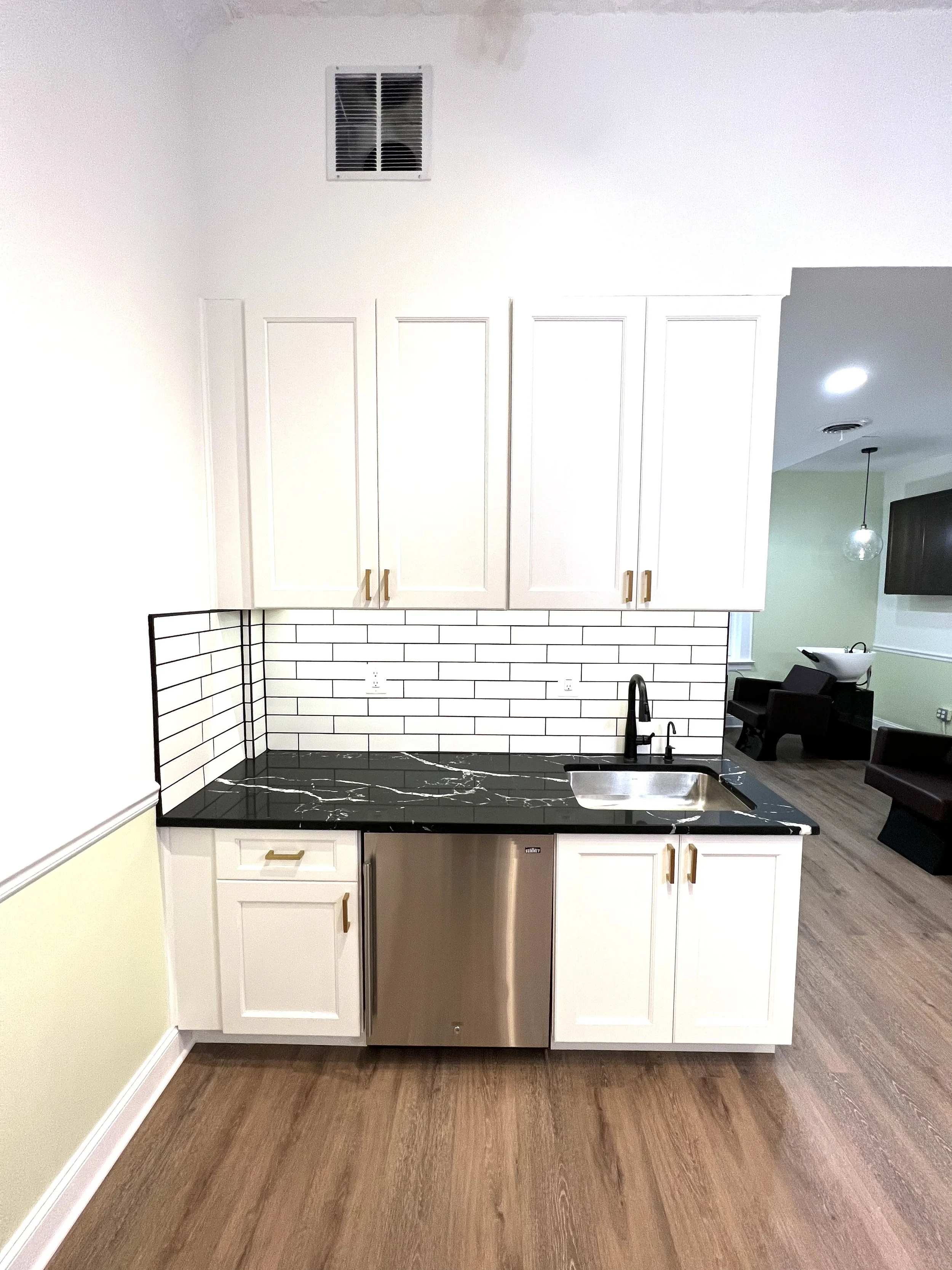 Kitchen with white cabinets, black marble countertop, white subway tile backsplash, stainless steel mini fridge, and black faucet.
