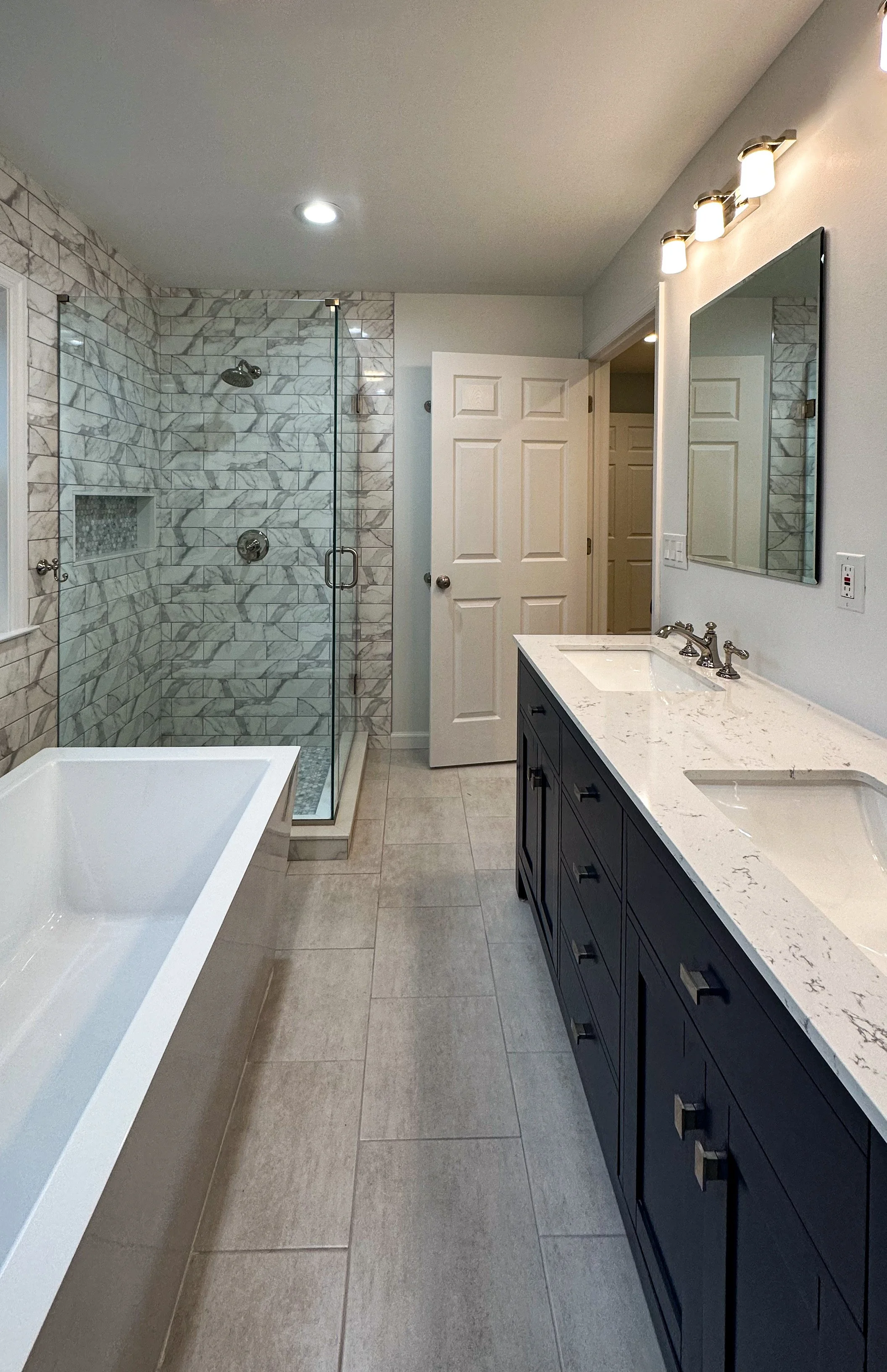 Modern bathroom with a walk-in shower with marble tiles, a bathtub, a dark blue vanity with a marble countertop, and a mirror above the sink.