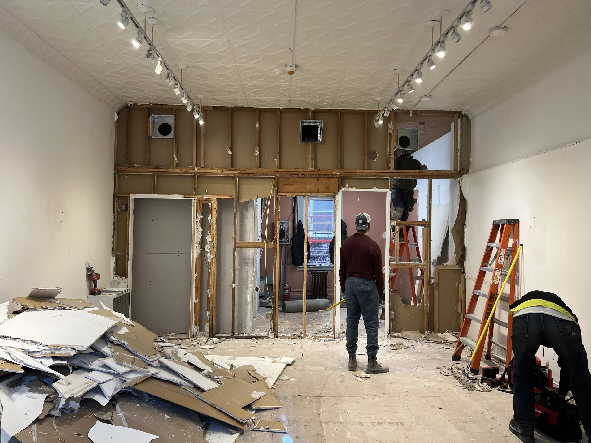 Interior of a building under renovation with exposed framing, construction workers, and construction tools.