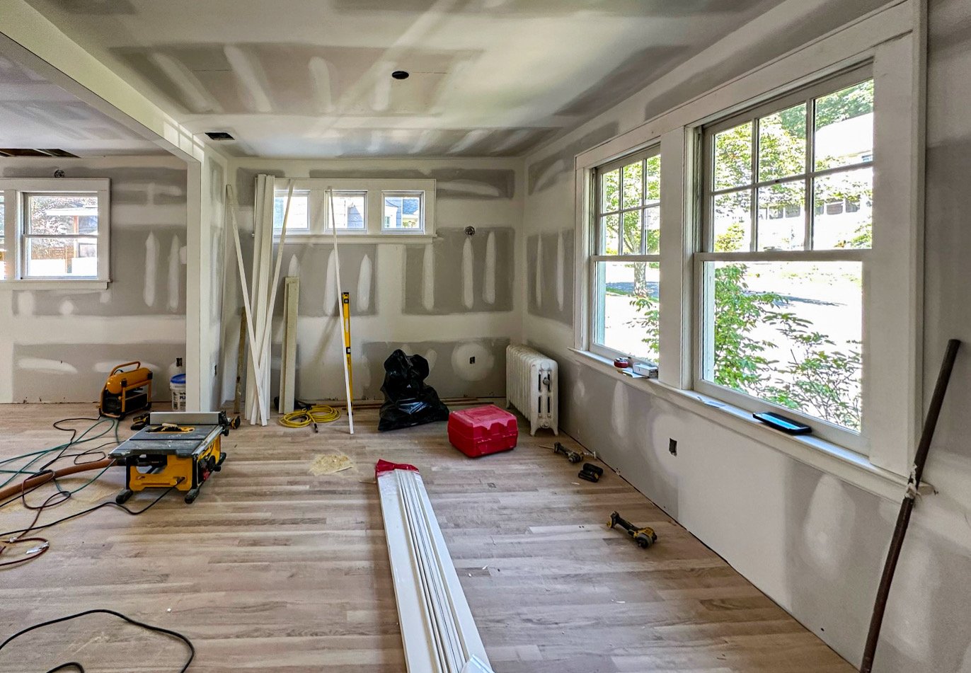 Room under construction with drywall installed, large windows, construction tools, materials, and scattered equipment.