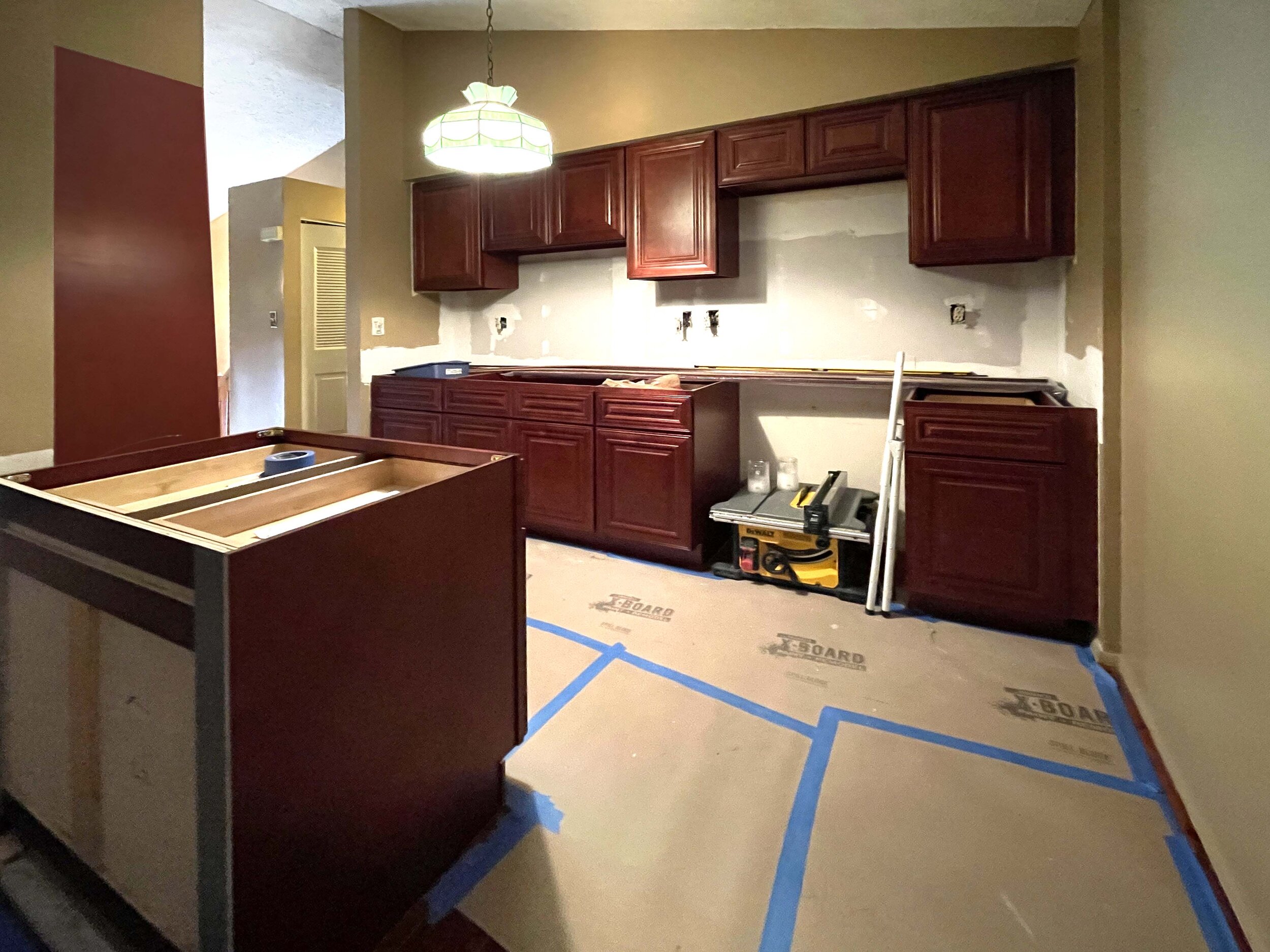 Kitchen under renovation with partially installed dark wood cabinets, a ceiling light, and construction tools on the floor.