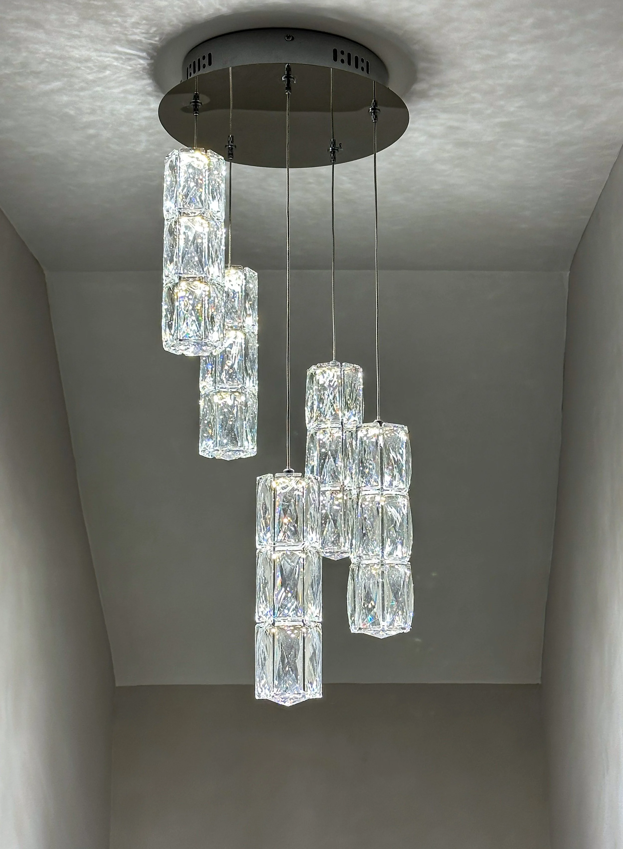 Modern chandelier with multiple hanging glass or crystal rectangular pendants illuminated against a neutral ceiling.
