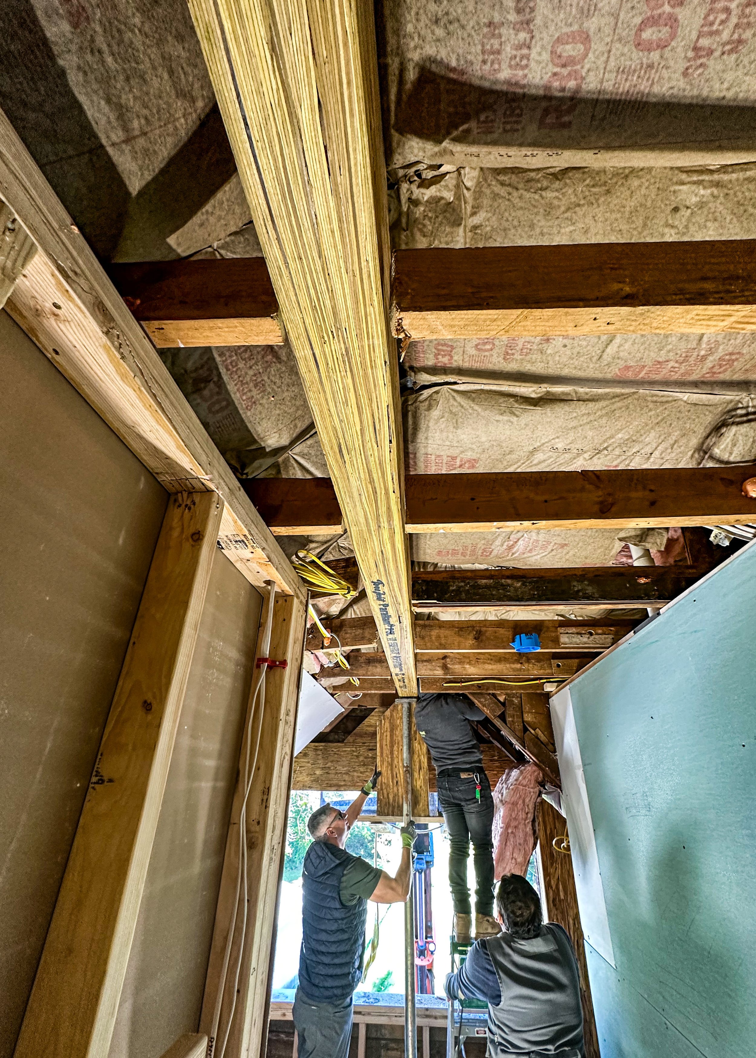 Three workers inside a house under renovation, installing or working on electrical wiring in the ceiling.