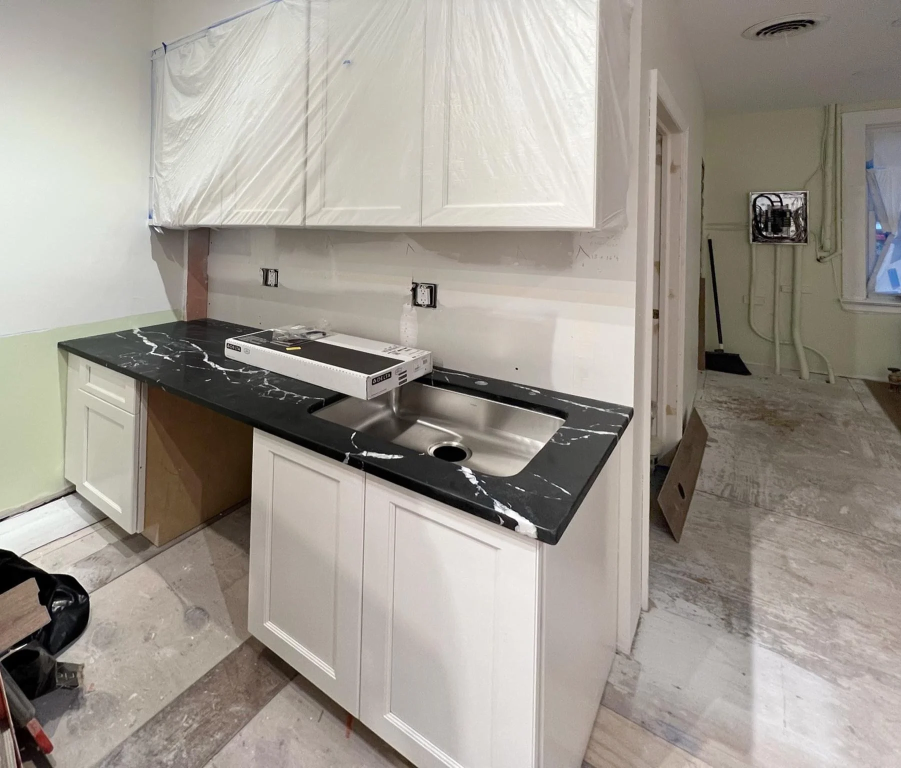 Kitchen under construction with white cabinets, black marble countertop, and a stainless steel sink.