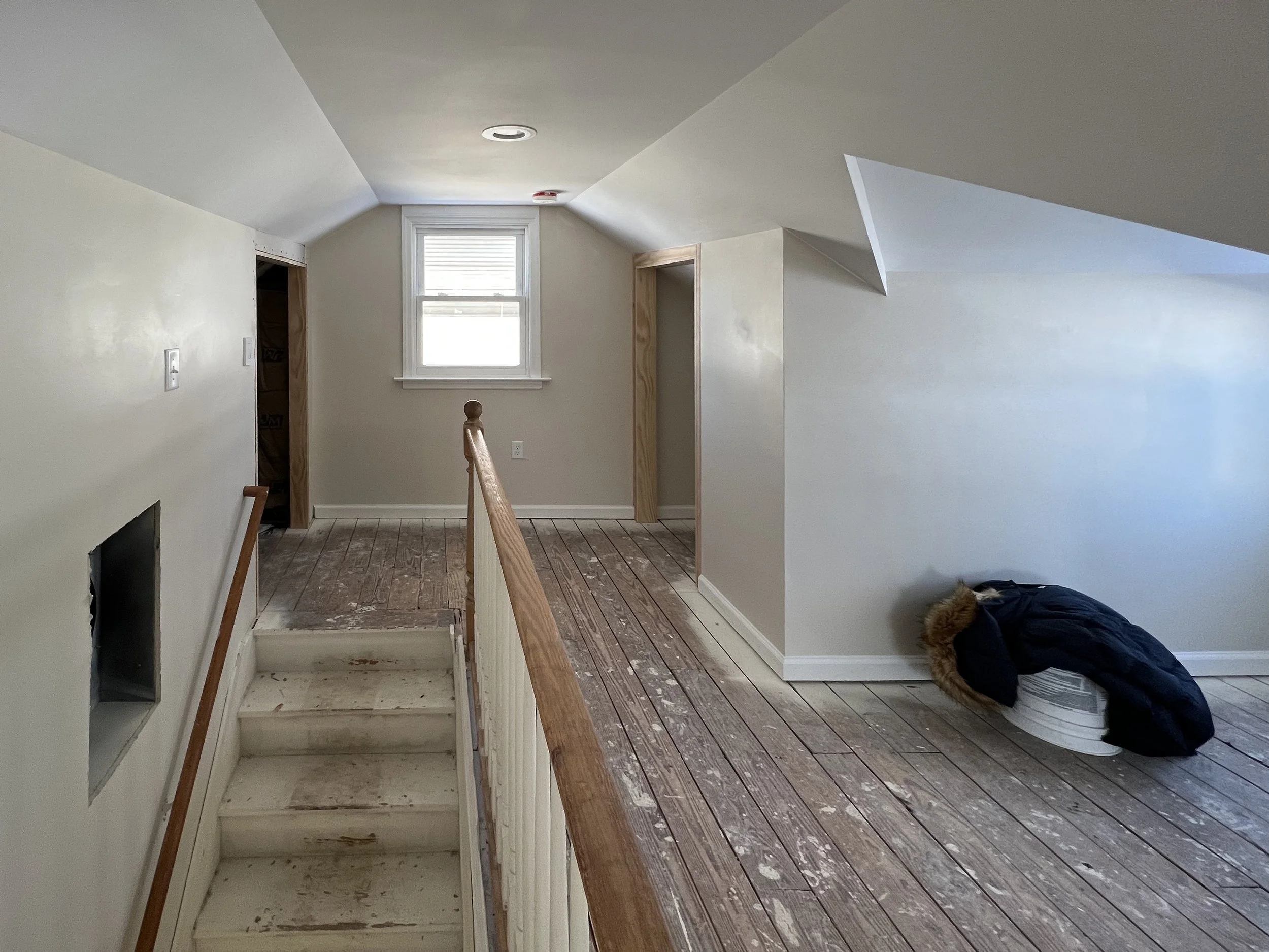 Interior of an unfinished room with a staircase, a window, and a construction worker working on the floor.