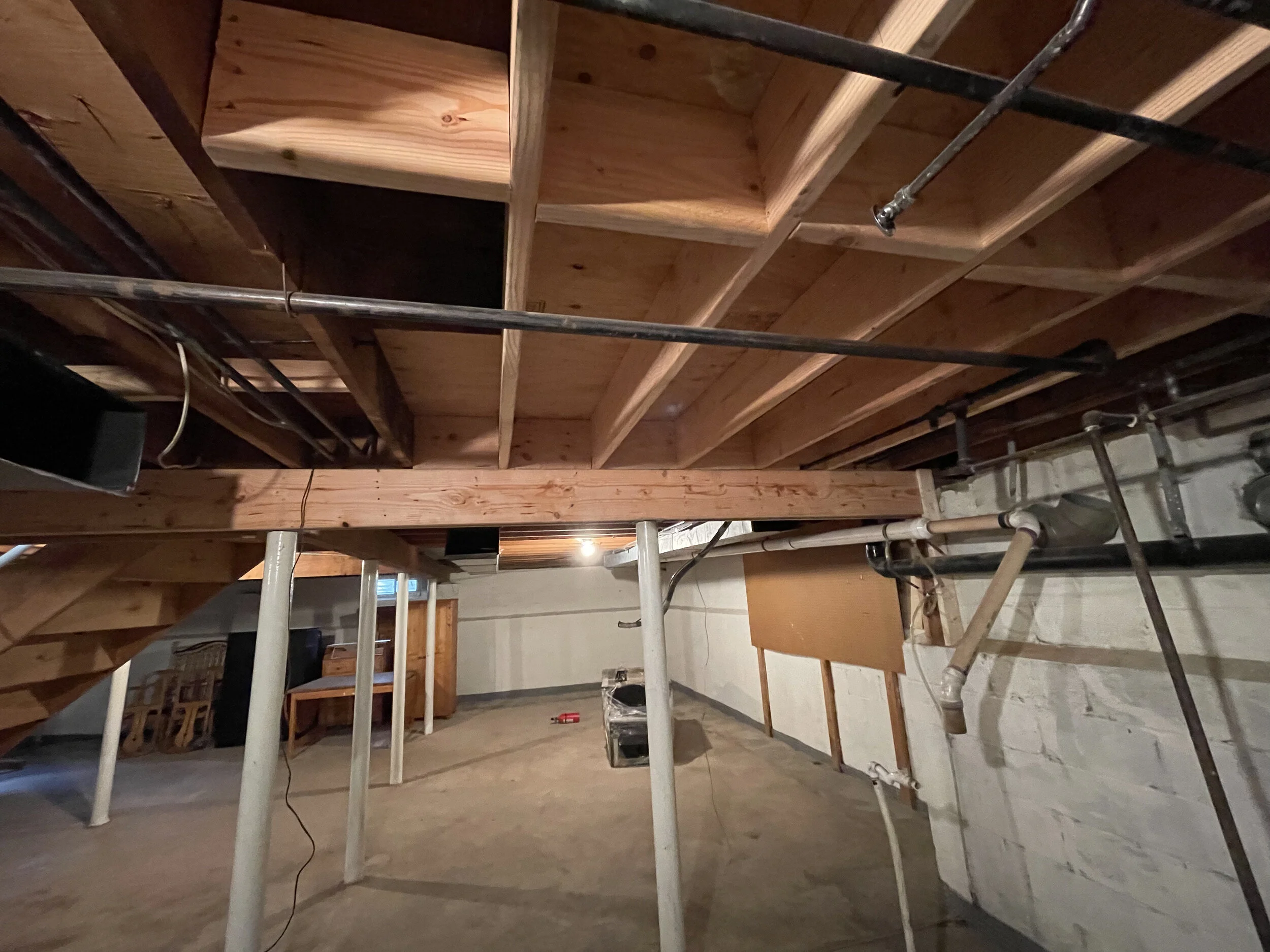 Indoor construction site with wooden framing and pipes, electrical wiring, and a concrete floor.