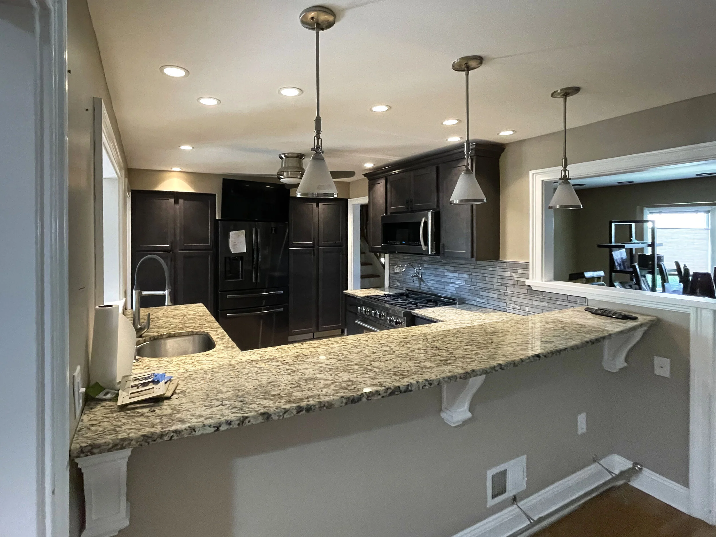 Kitchen with granite countertops, dark wooden cabinets, a black refrigerator, stainless steel appliances, and pendant lights.