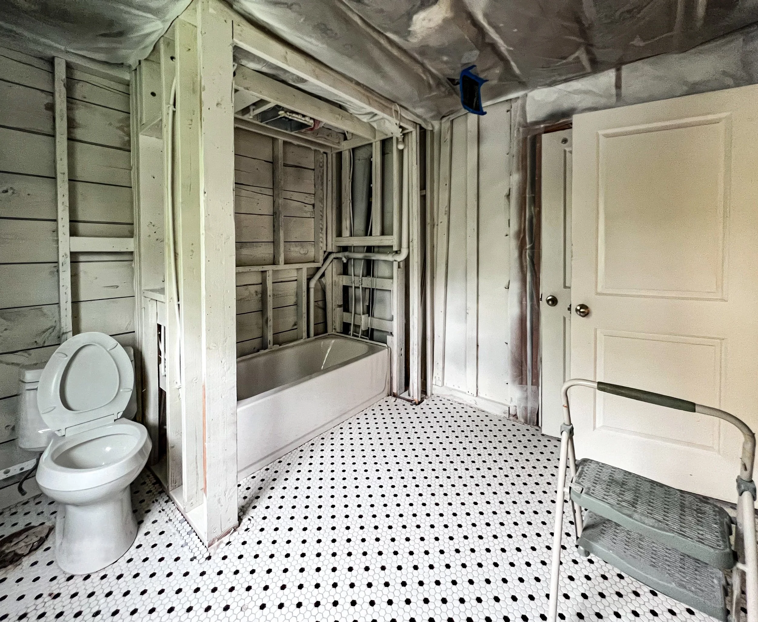 Bathroom under renovation with an exposed frame shower area, a toilet, a walker, and a black and white mosaic tile floor.