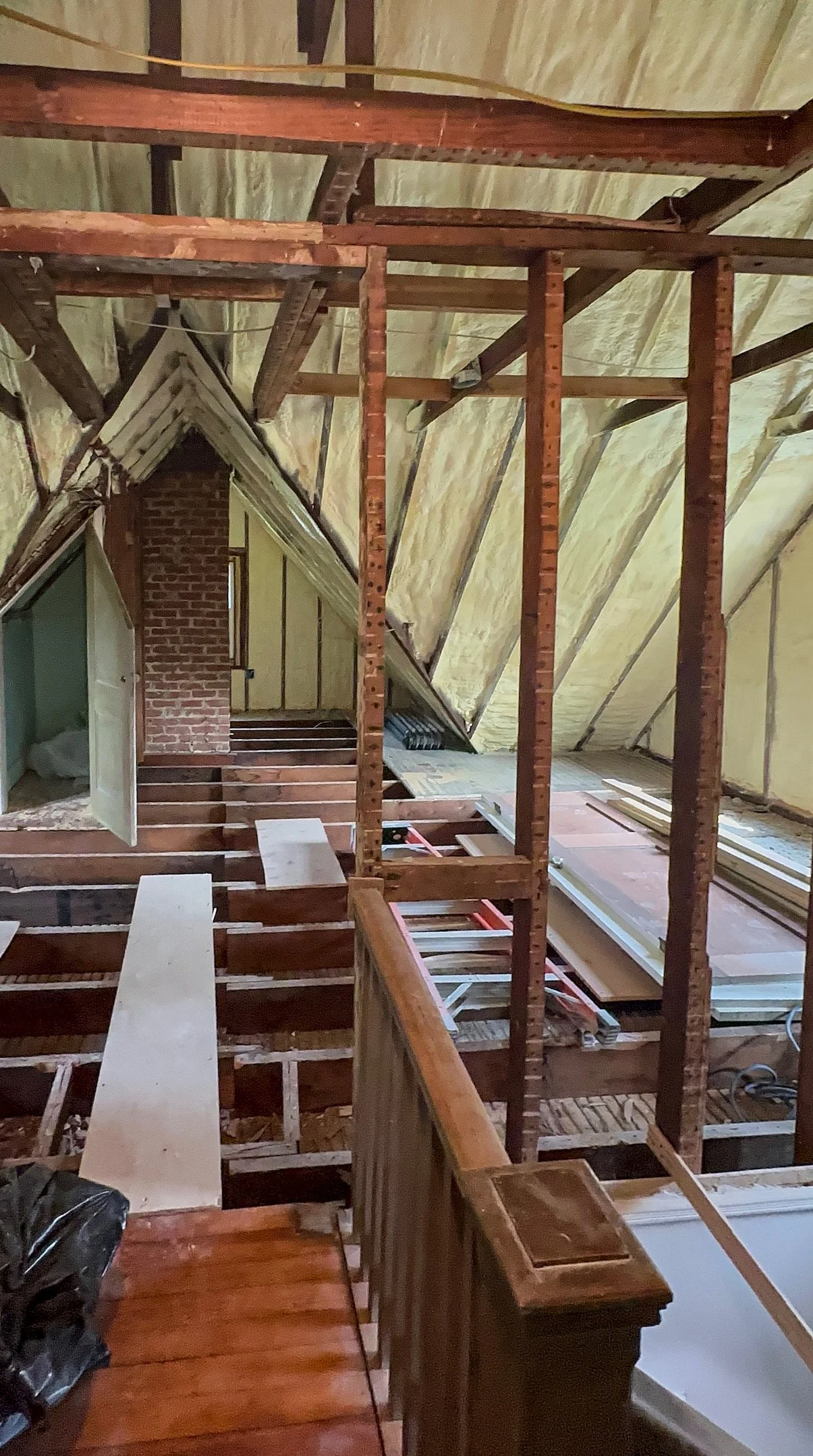 Attic under renovation with exposed wooden beams, insulation, and partially installed flooring, showing the framework and construction materials.