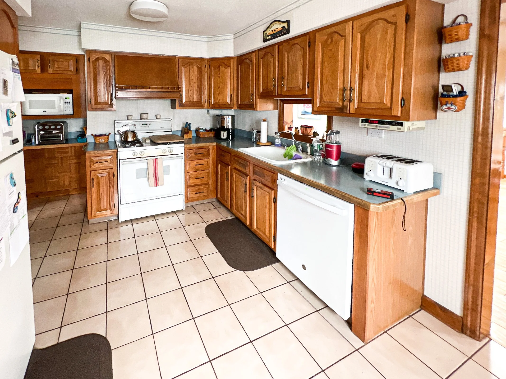 Kitchen with wooden cabinets, white appliances, tiled floor, and various small appliances on the counter, including a toaster and coffee maker.