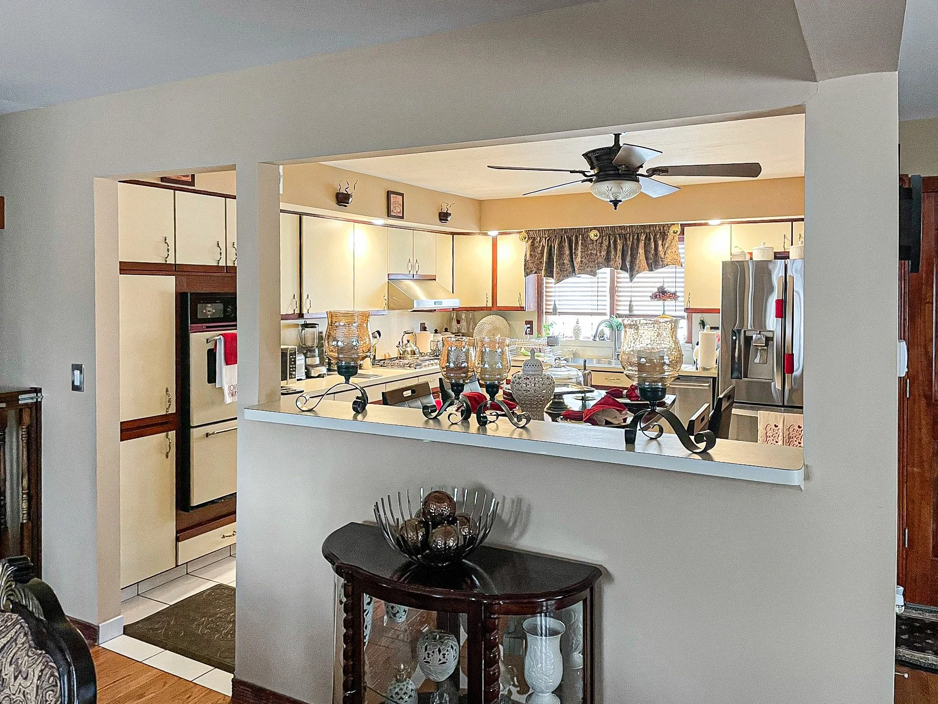 Kitchen with beige cabinets, refrigerator, stove, microwave, and window with valance. Decor includes lamps, vases, and Christmas stockings.