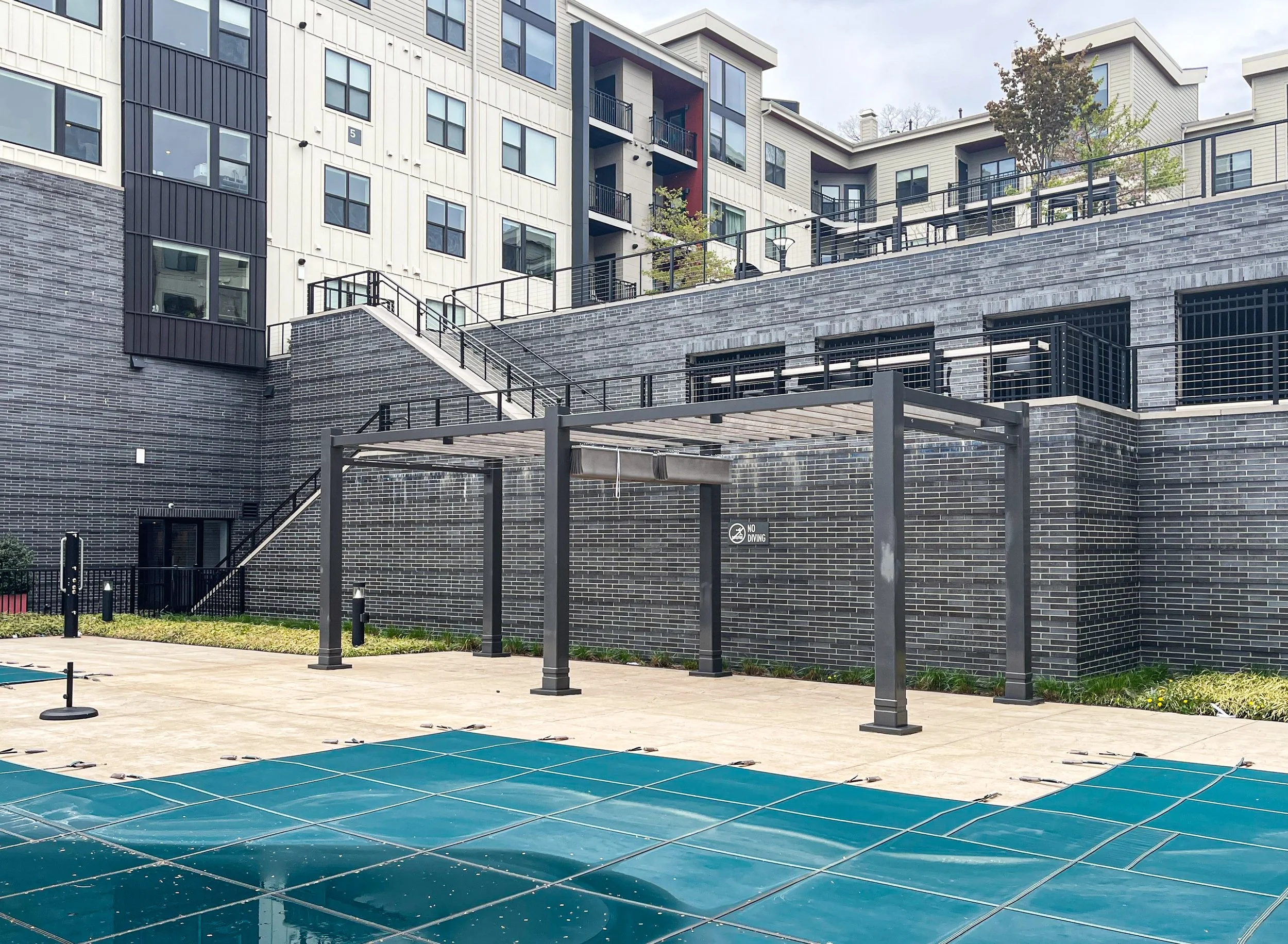 Empty swimming pool covered with a green solar cover at a modern apartment complex with brick and white siding exterior.