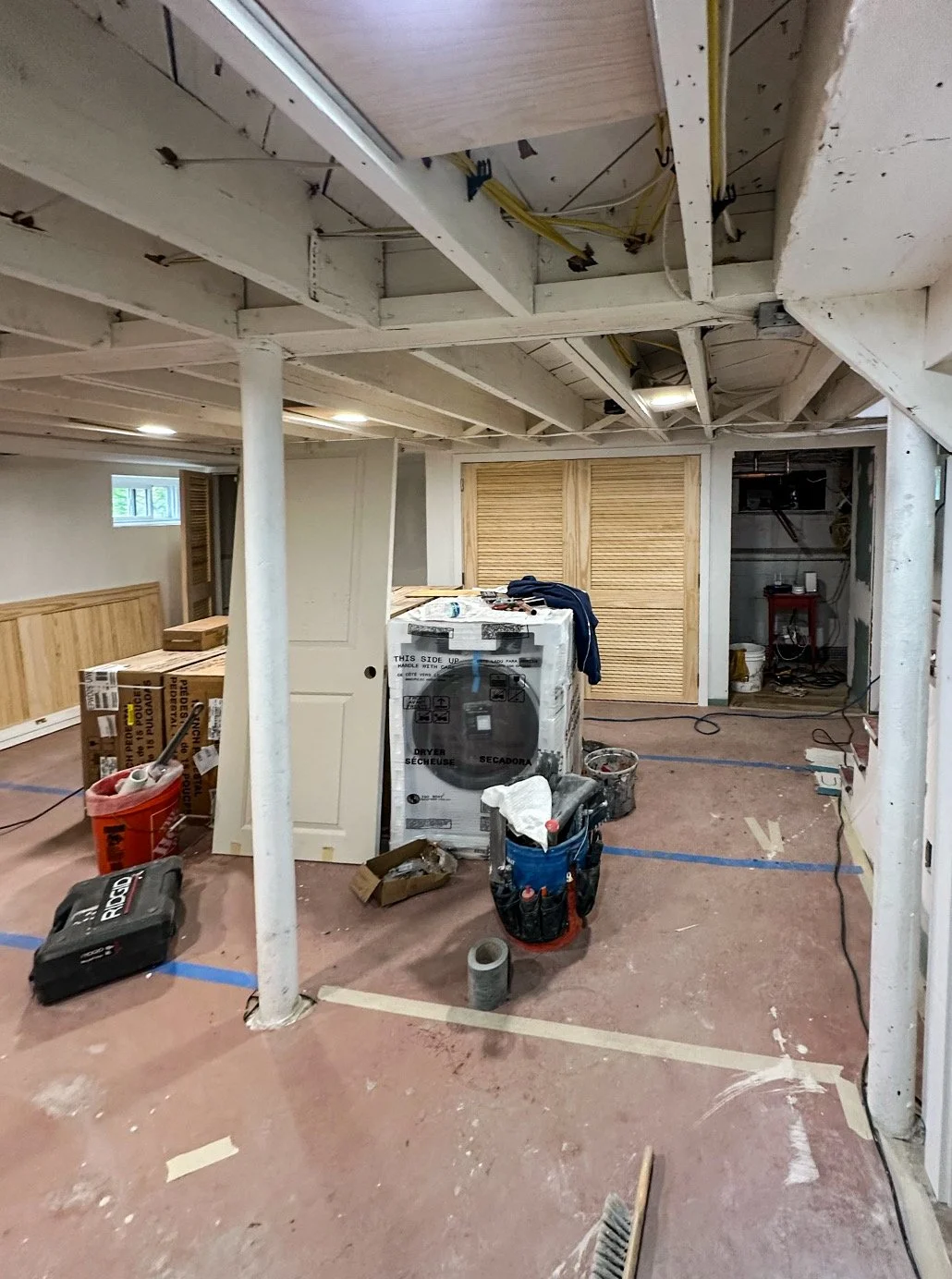 Interior of a basement under construction with exposed beams, construction tools, and materials scattered on the floor.