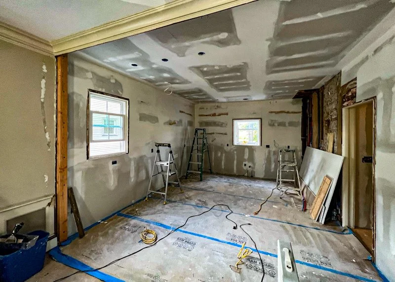 Room under renovation with drywall installation, construction tools, ladders, and unpainted walls.
