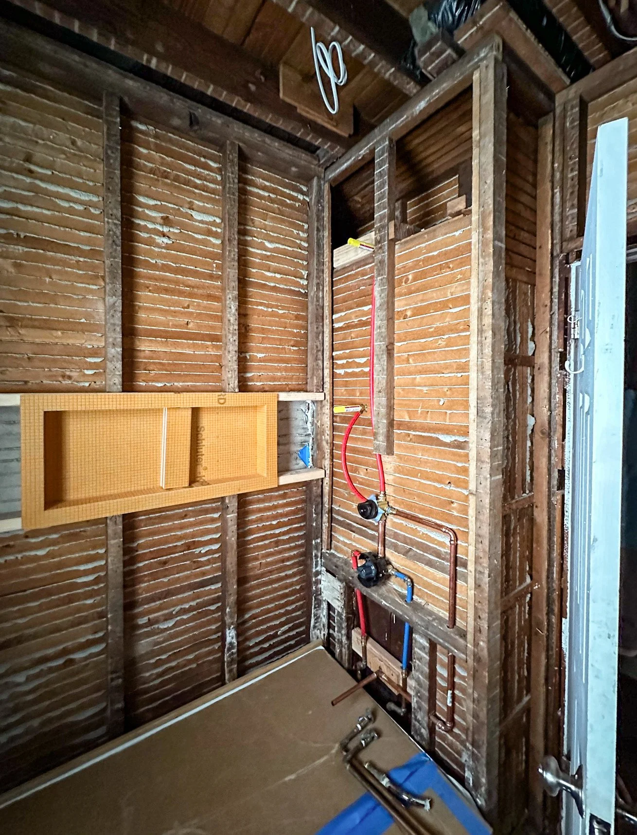 Unfinished room with exposed wooden framing, plumbing, and a pegboard on the wall.